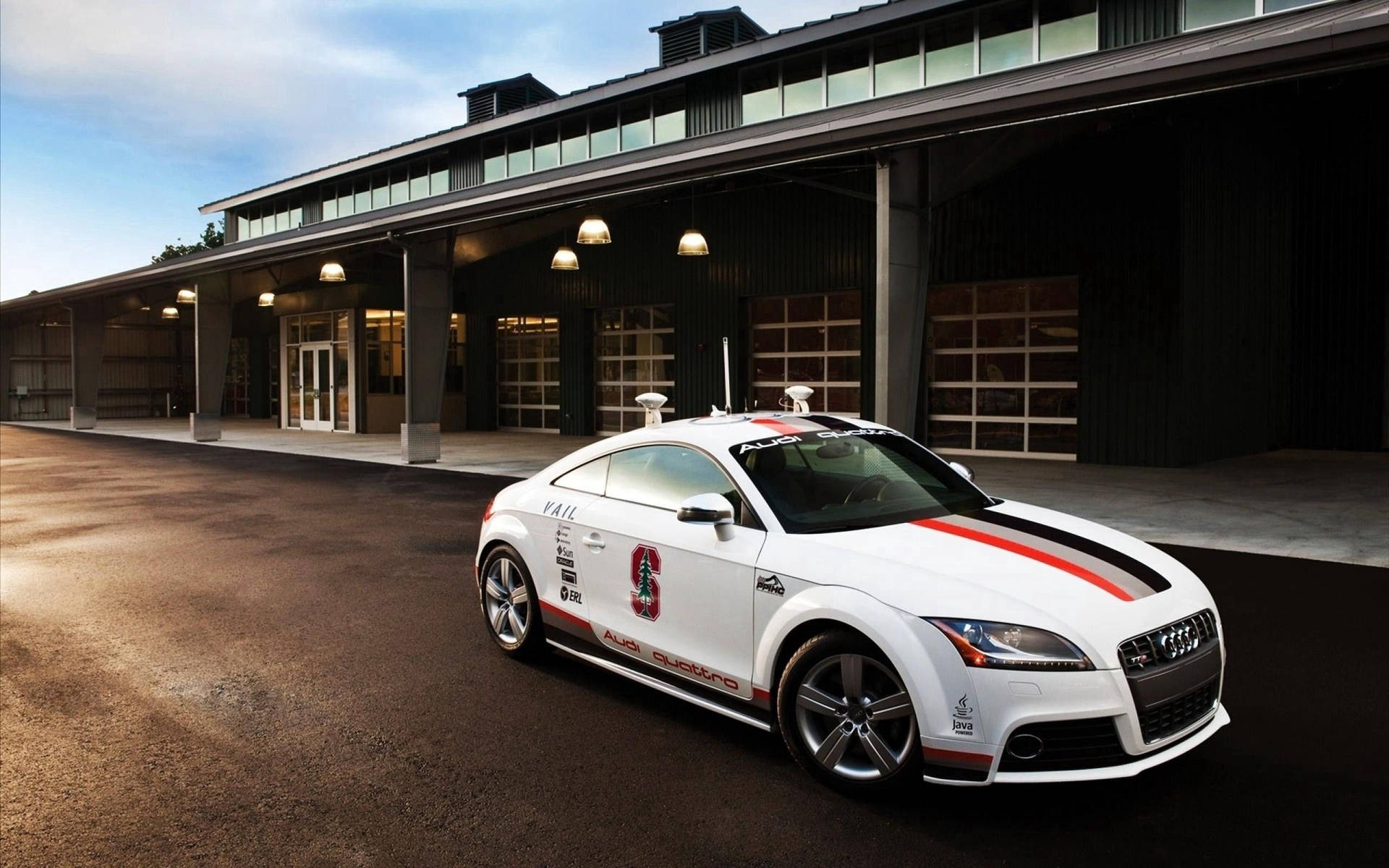 白色奧迪TT賽車帶紅色條紋，停在工業建築前，日落時分。