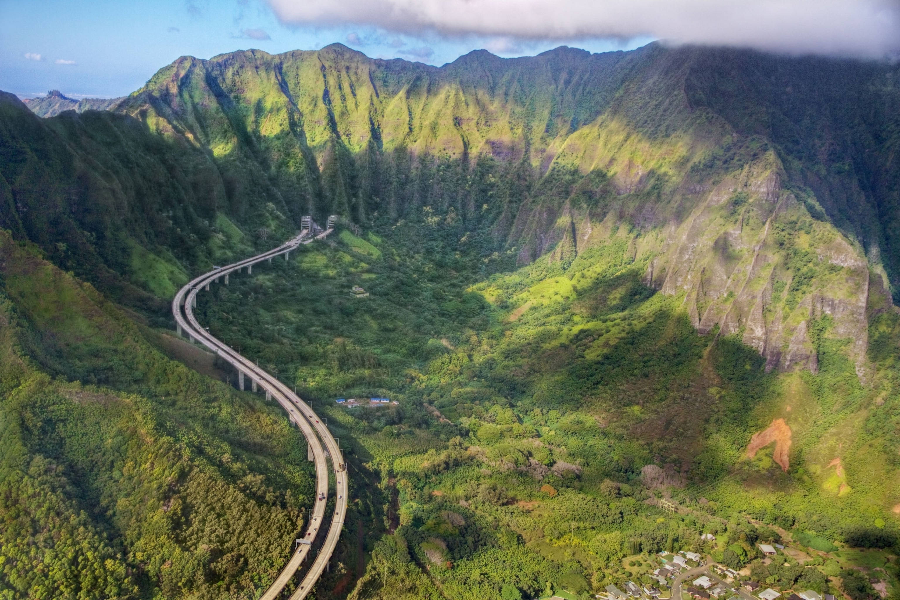 奧阿胡島高速公路鳥瞰 壁紙 — 一條蜿蜒的高速公路在部分多雲的天空下蜿蜒穿過鬱鬱蔥蔥的綠色山脈。