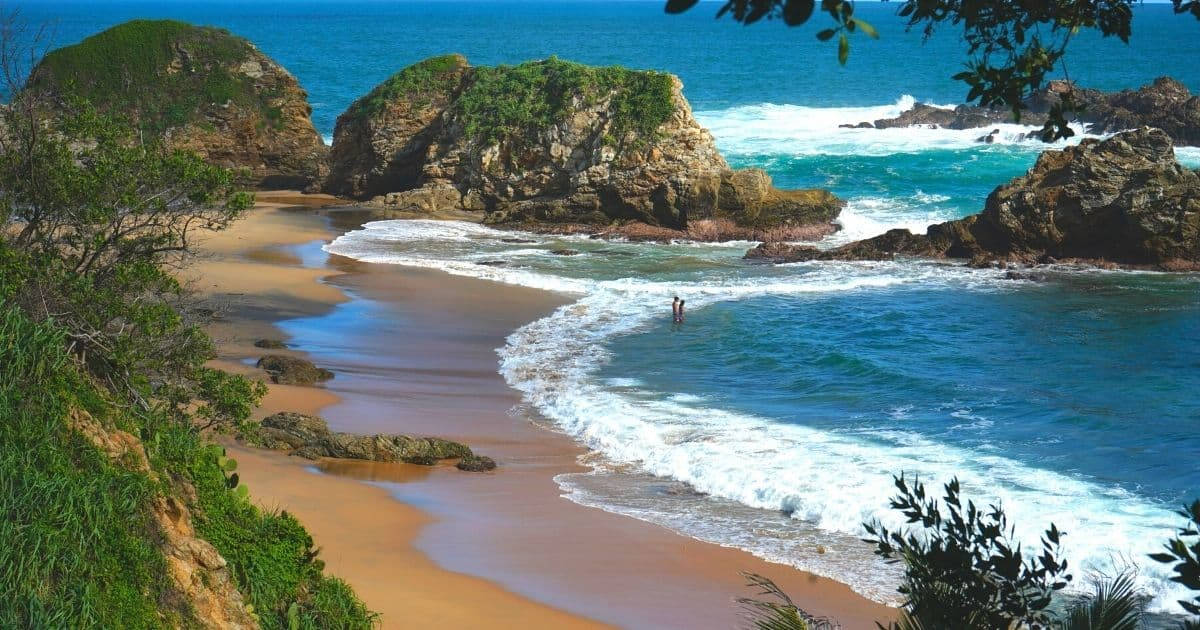 人在綠色懸崖附近的沙灘海洋波浪中游泳