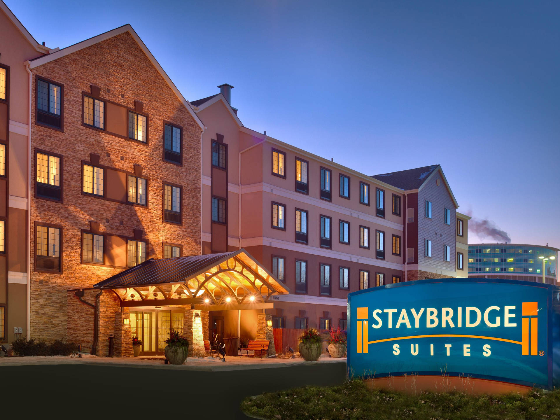黃昏時的 Staybridge Suites 酒店，窗戶亮燈，入口有遮陽篷。