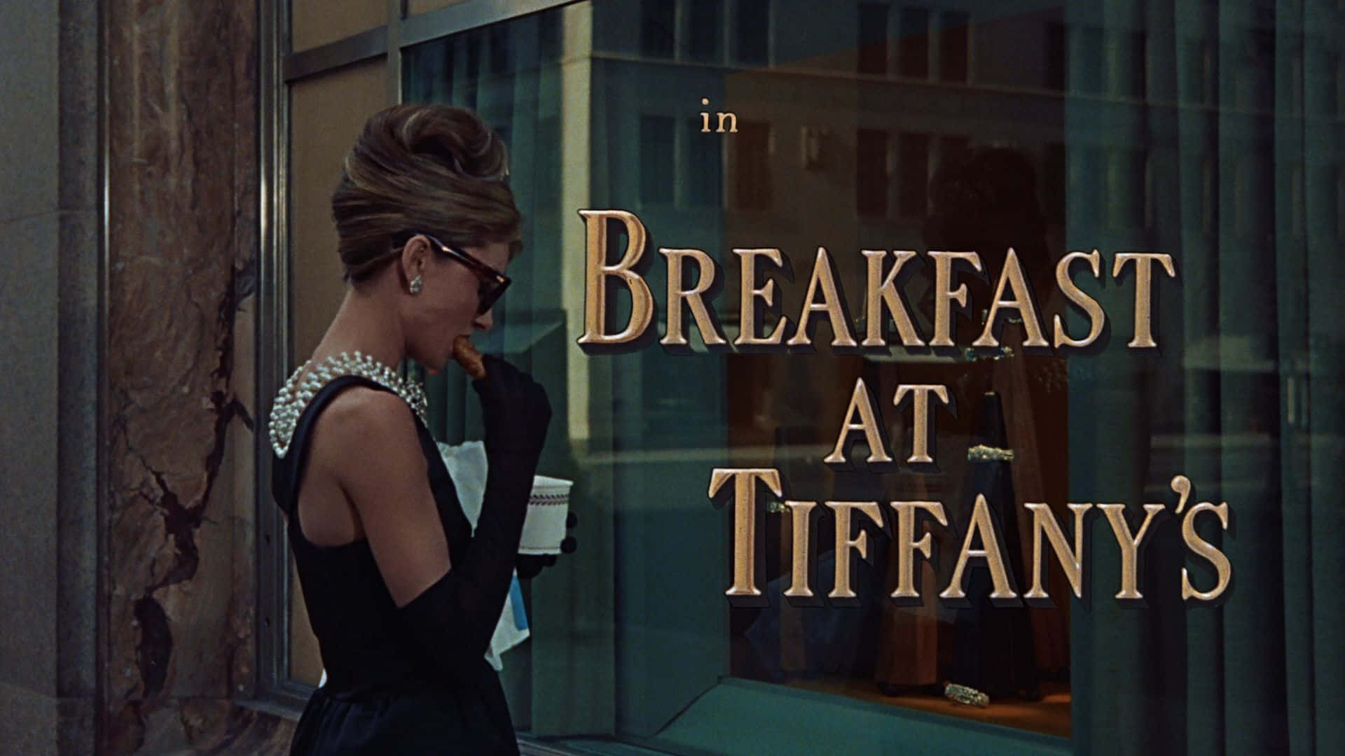 身穿黑色連衣裙和珍珠的女性在Tiffany's店外手持咖啡。