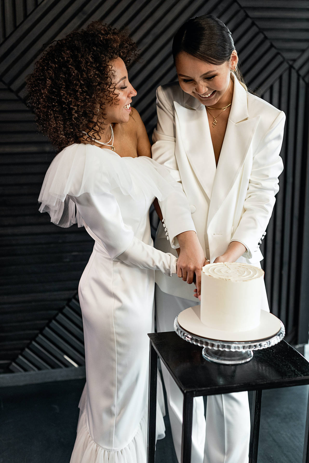 兩位身穿白色婚紗的新娘在室內切結婚蛋糕。