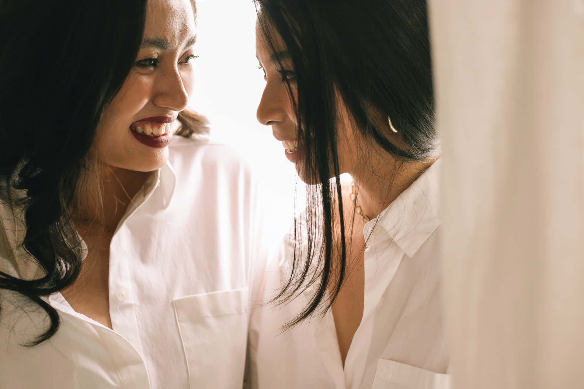 兩位身穿白恤衫的女性在柔和光線中溫暖地微笑相對。