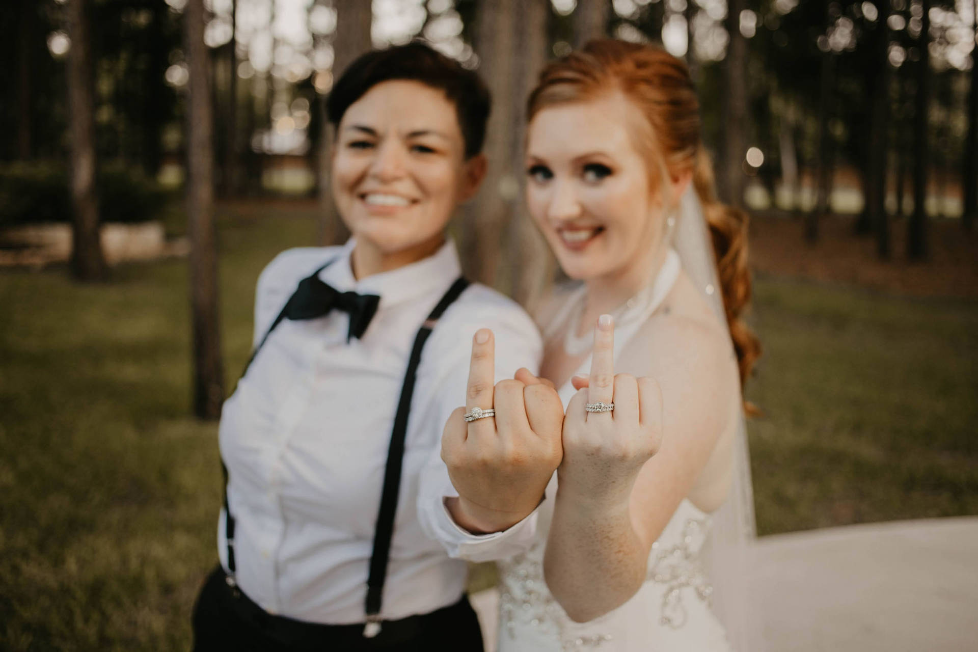 兩位快樂的新娘在森林中夕陽下展示結婚戒指。