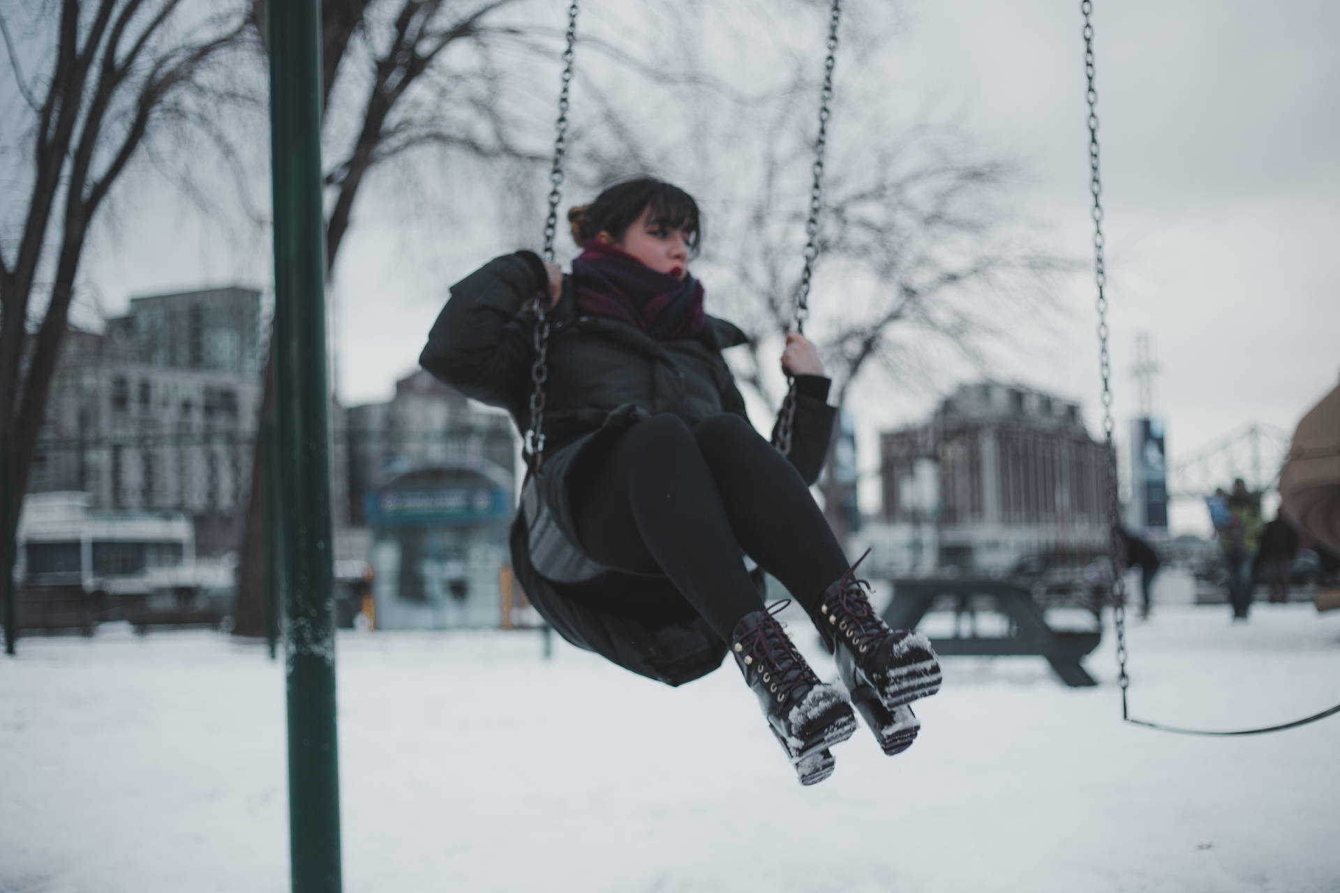 在雪地城市公園中穿著冬季衣服坐在鞦韆上的人