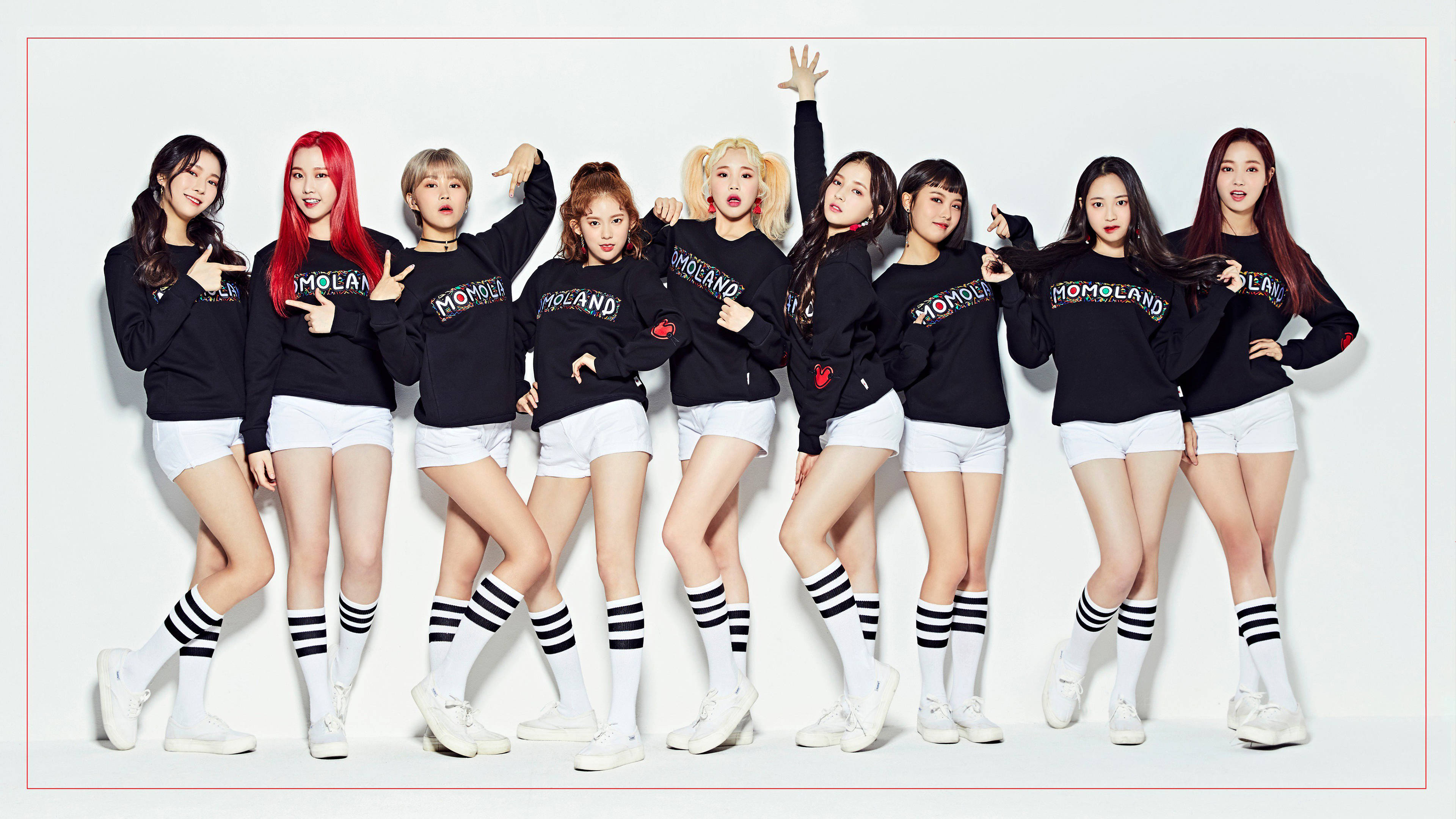 女子團體南西 Momoland 高畫質 壁紙 — 九位時尚女偶像自信地擺姿勢，身穿相配的黑色連帽衫、白色短褲和條紋襪子，背景是純白色。
