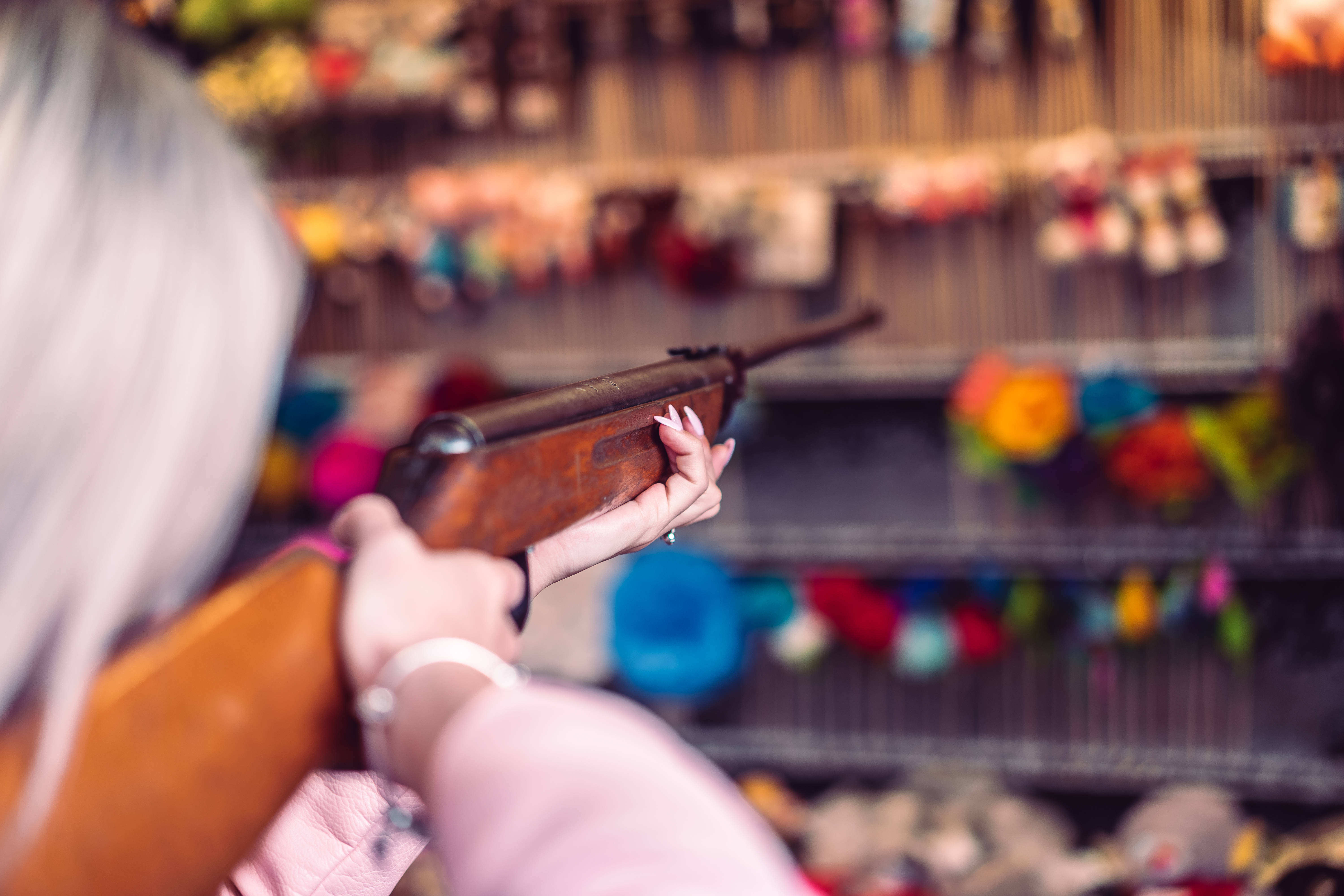 女子射擊步槍 壁紙 — 一位銀髮人士在色彩繽紛的玩具店中手持一把復古木製步槍，身後是模糊的貨架。