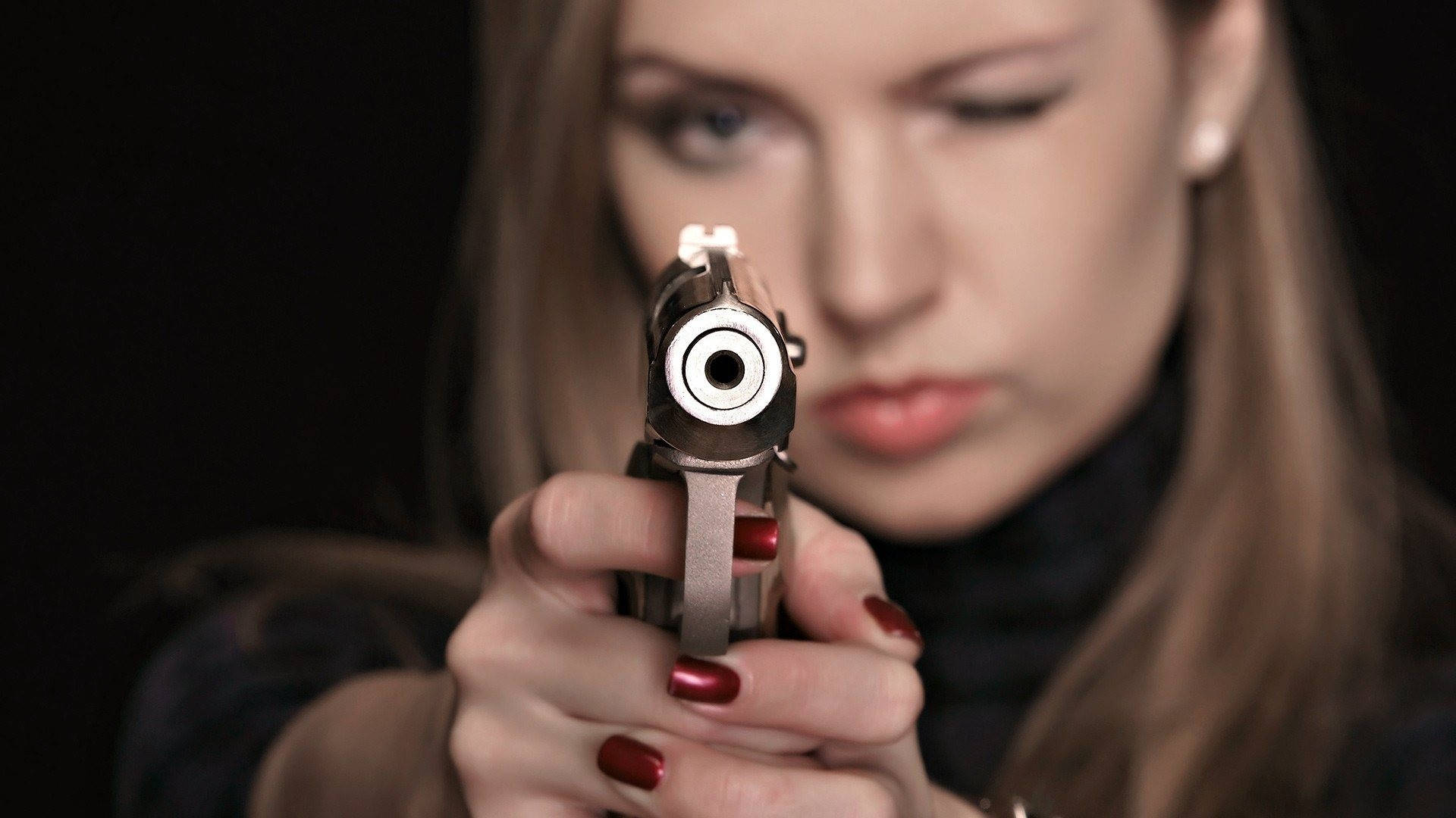 女子指槍射擊 壁紙 — 一位紅指甲的女性在黑色背景下直接將手槍瞄準觀眾。