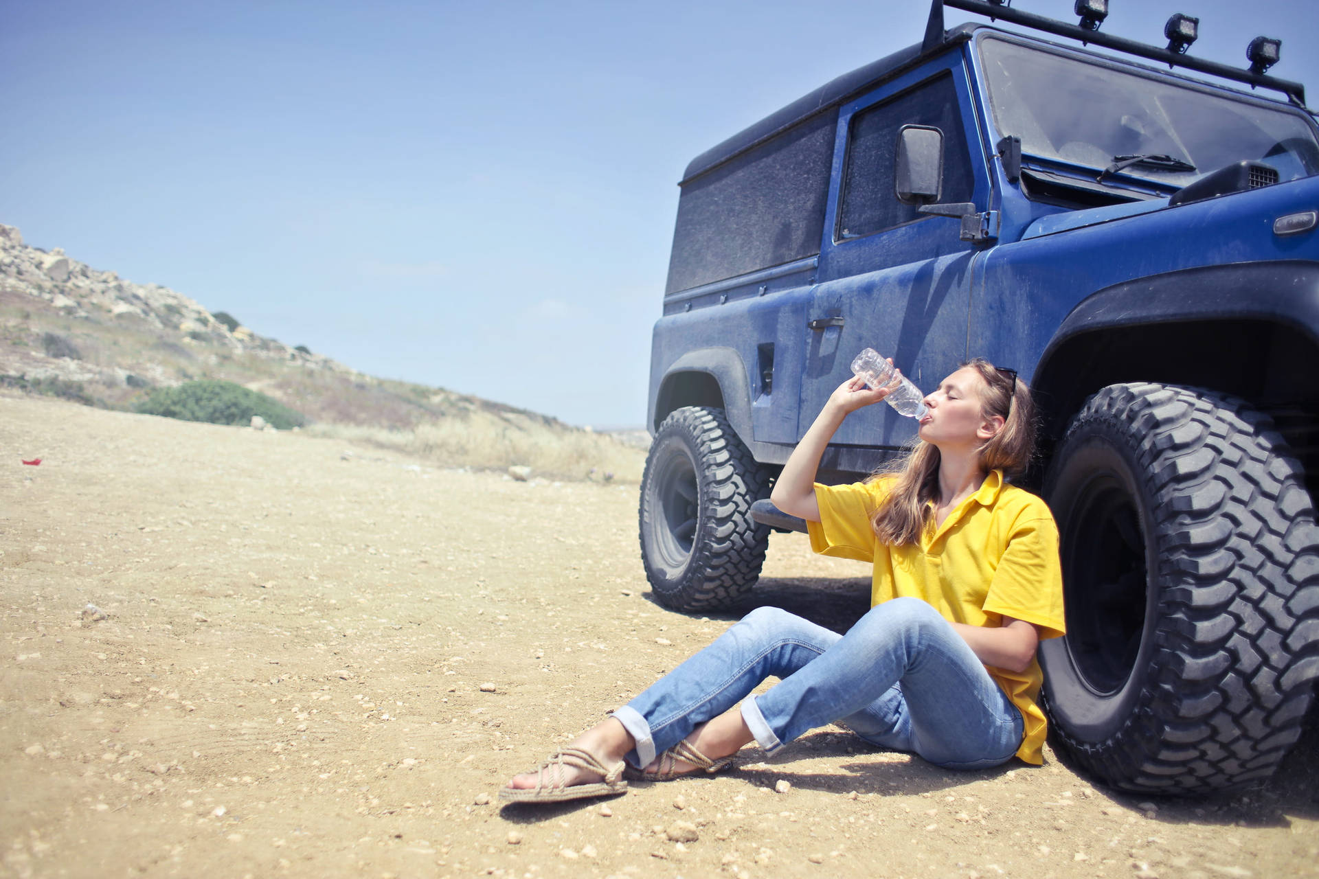 女子在沙漠中藍色越野車旁喝水