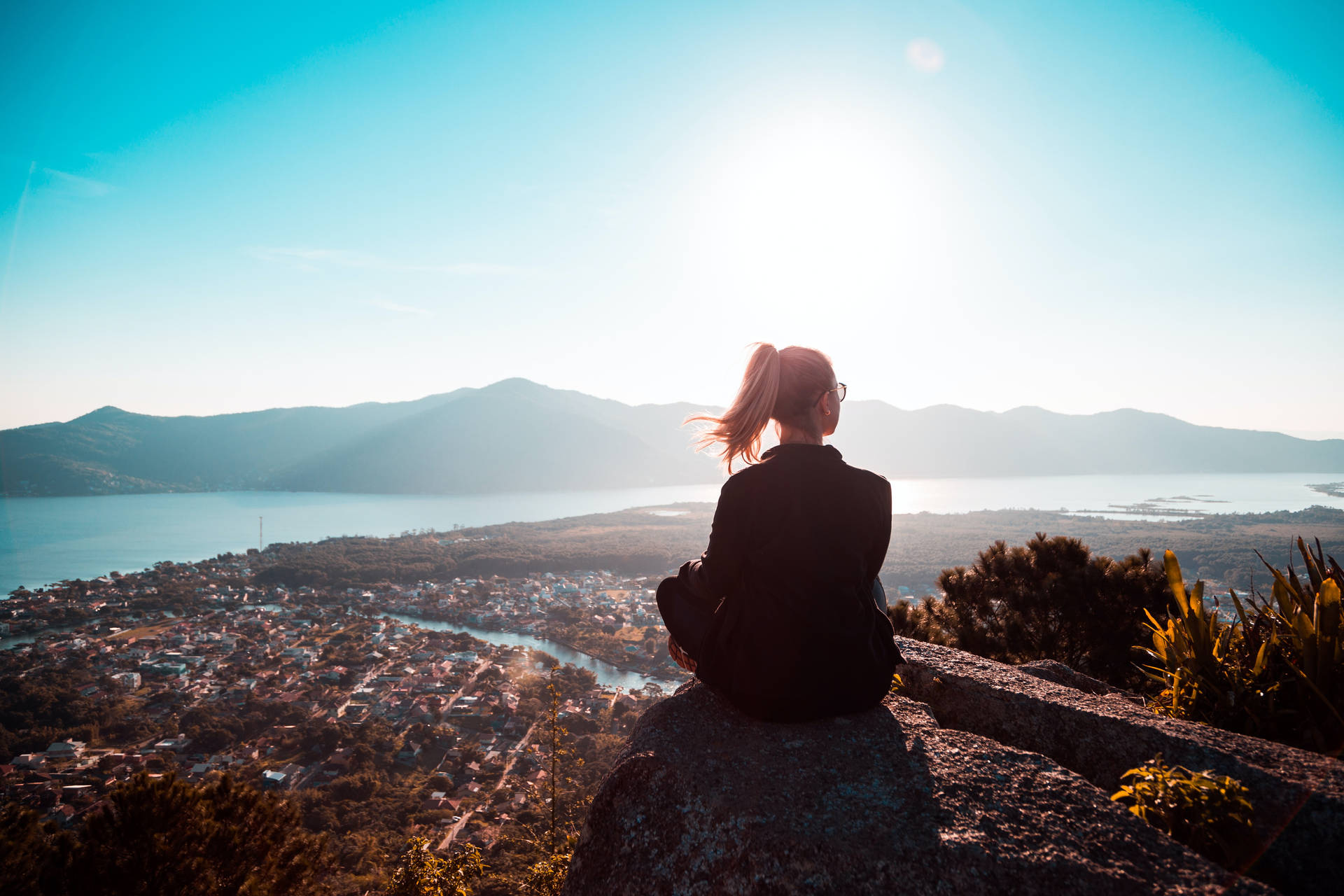 人坐在懸崖邊緣，俯瞰日落時分的海岸小鎮。