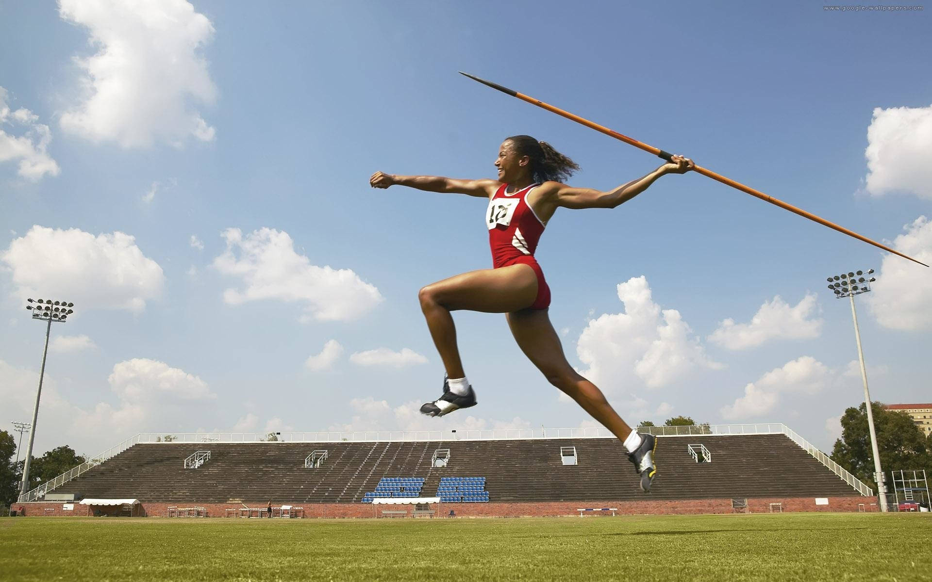 身穿紅色運動服的女運動員在陽光明媚的日子在戶外體育場擲標槍。