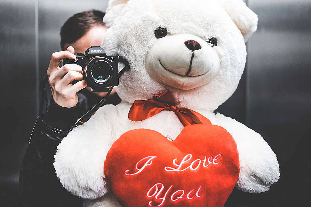 在電梯內拿著寫有 I Love You 心形枕頭的泰迪熊的人。