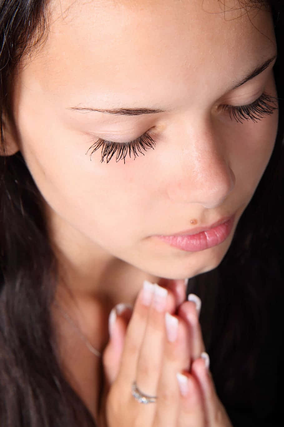 一個女人閉上眼睛，雙手合十祈禱。