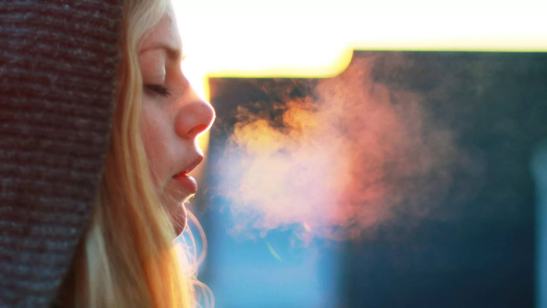 女子靜心深呼吸 壁紙 — 一名女性在溫暖的日落餘暉中呼出一團蒸氣，柔和的金色光線勾勒出她的側面輪廓。