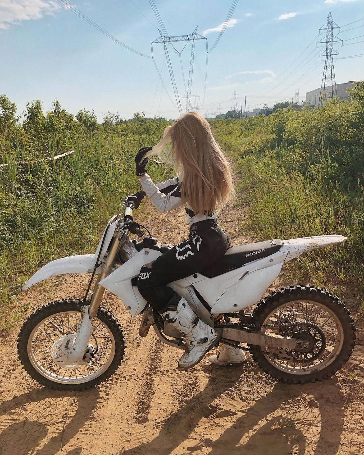 金髮女子穿著越野電單車裝備，在草地上騎白色越野電單車。 — 越野車 壁紙
