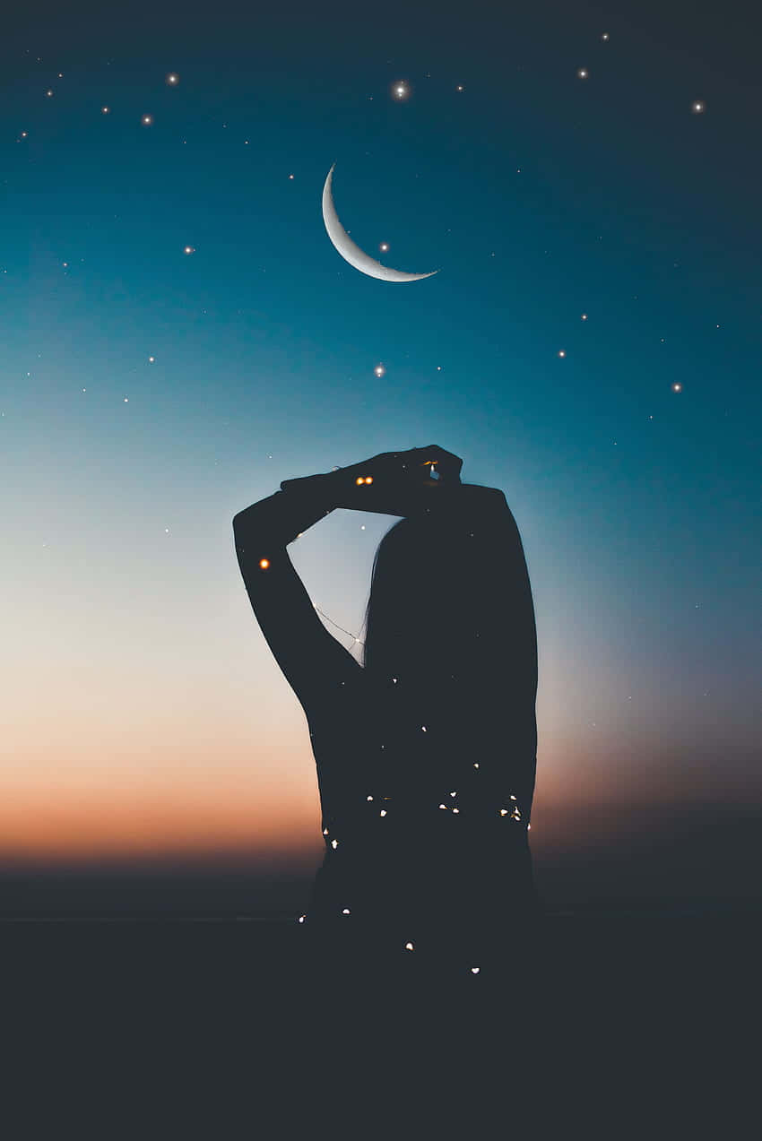 剪影中的人在黃昏時看著新月和星星。