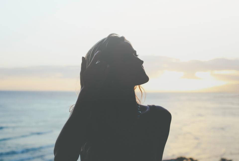 女人喺海邊日落中嘅剪影，手放喺頭度。