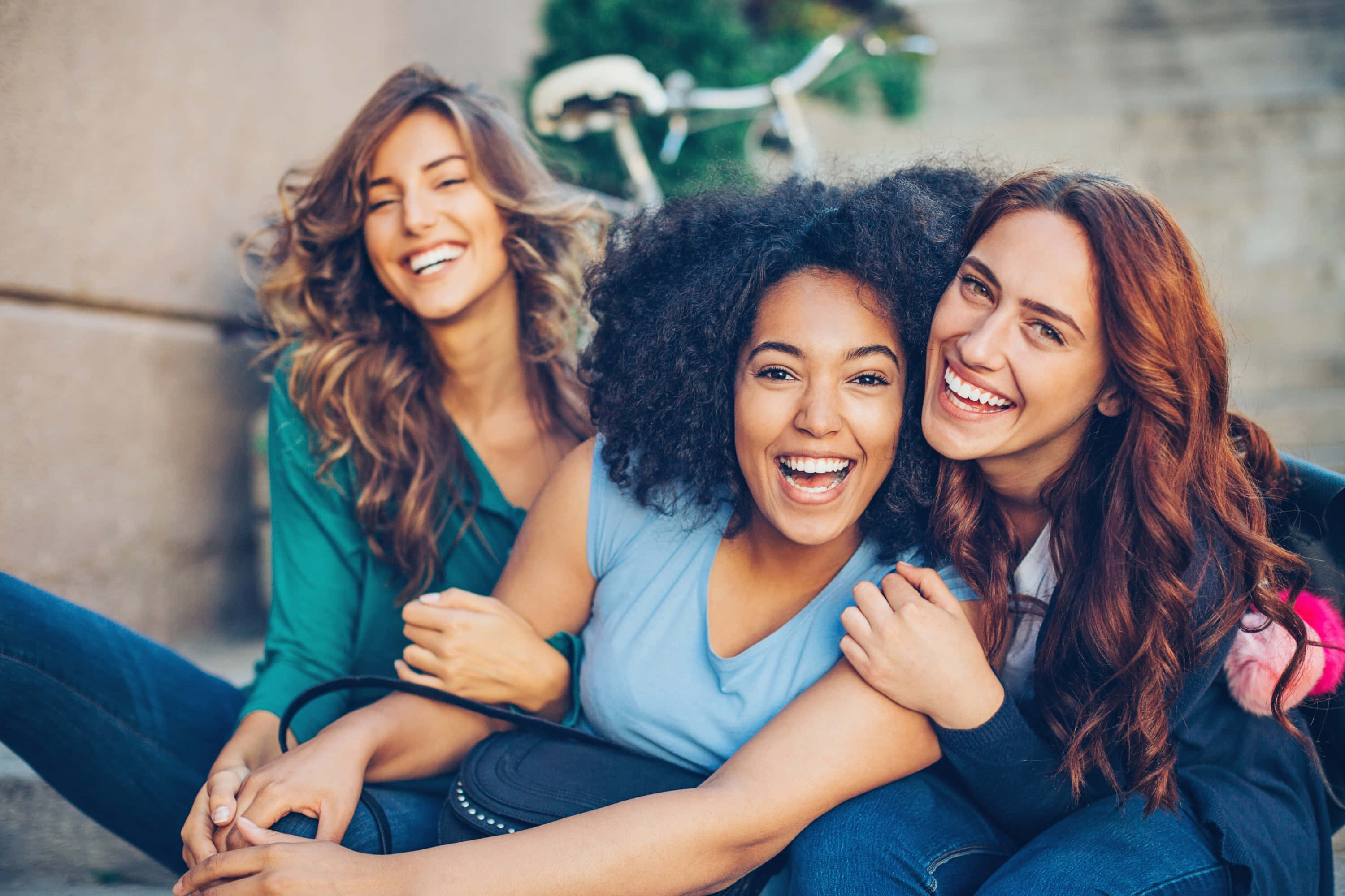 女孩力量——傳遞自信、喜悅與韌性！ 壁紙 — 三位快樂的女性在戶外笑著，背景有一輛單車。