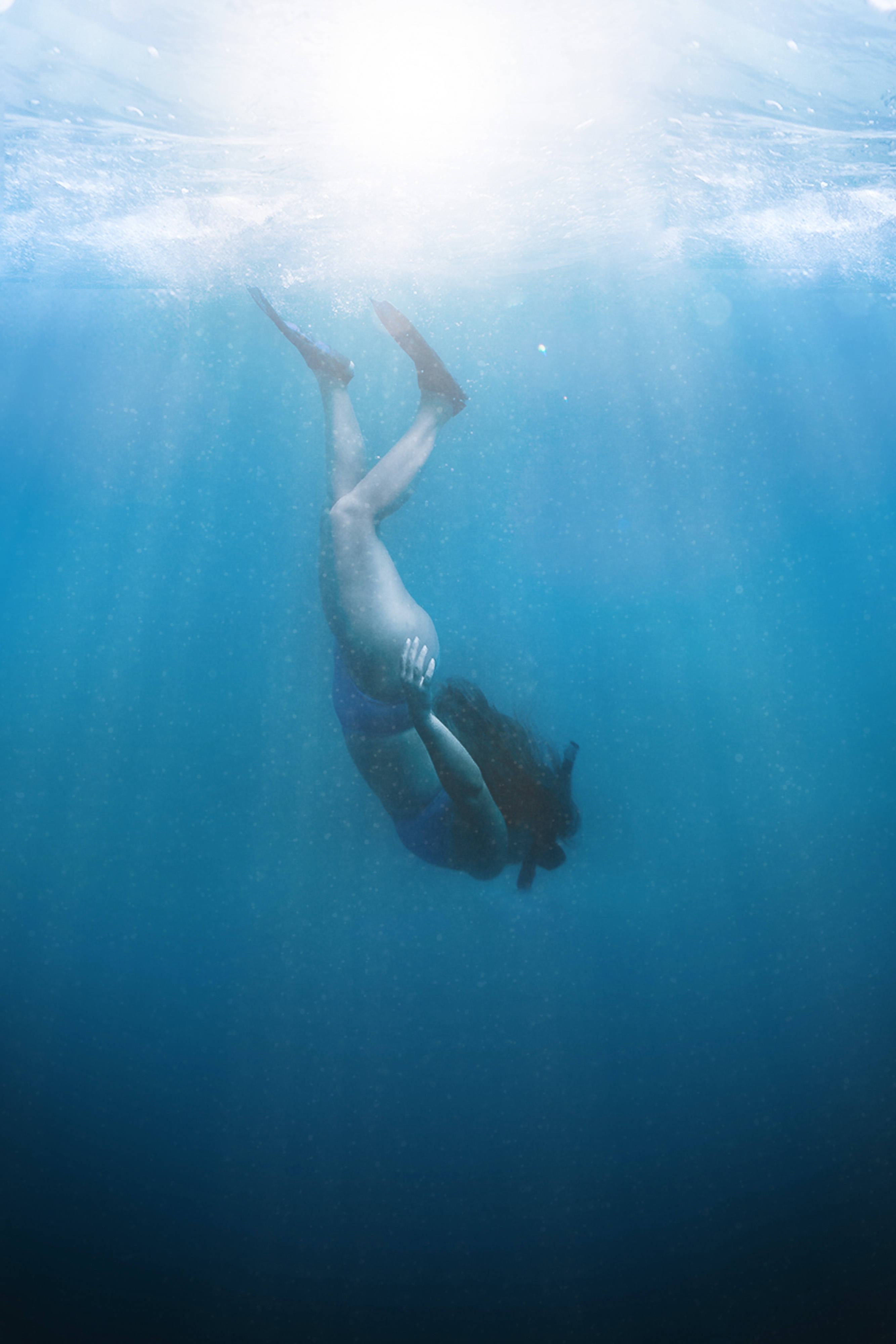 女孩向海底潛行 壁紙 — 一個人頭朝下潛入清澈的藍色海水，陽光從上方照射下來。