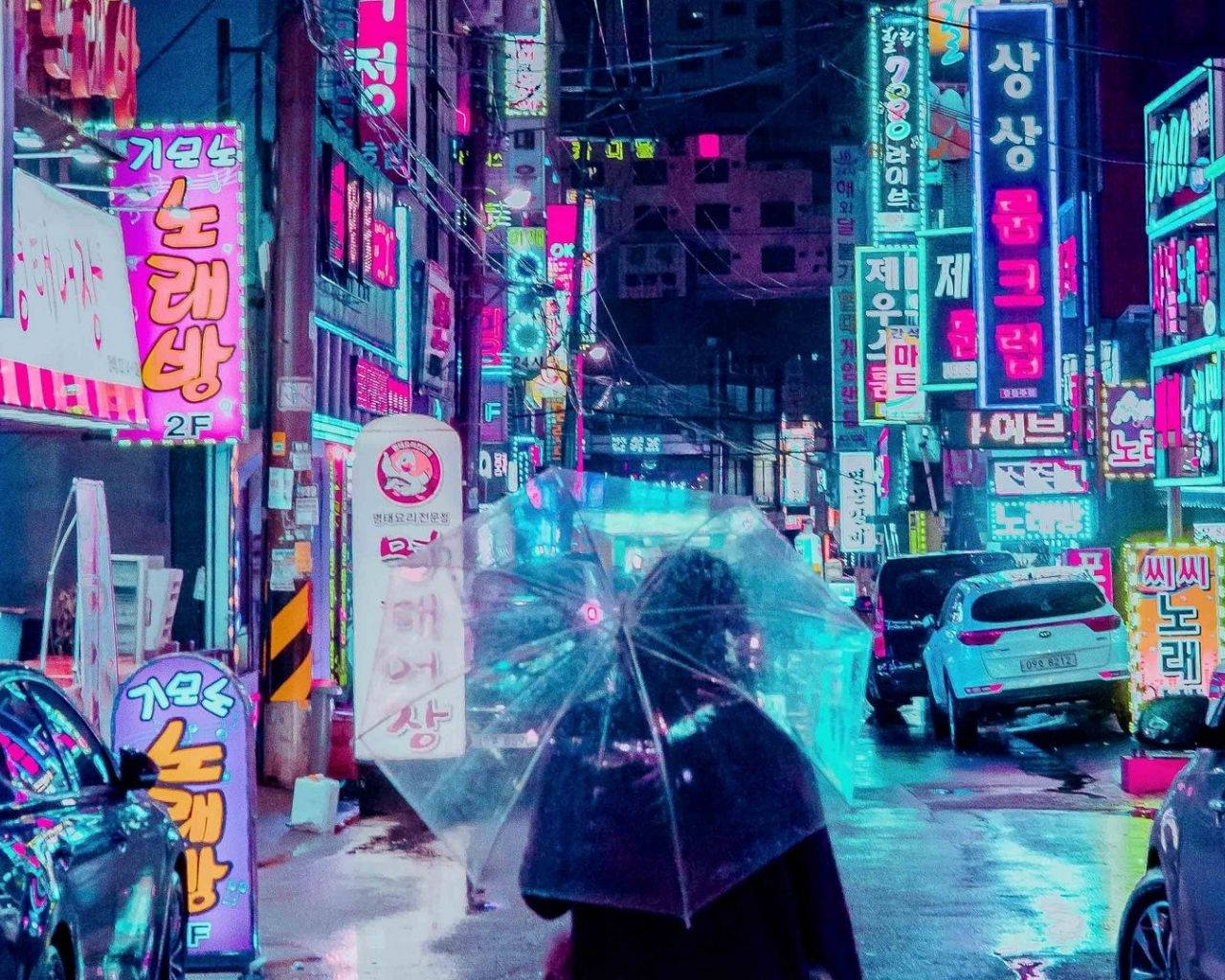 一個人拿著透明雨傘，在夜晚霓虹燈閃爍的雨街上行走。