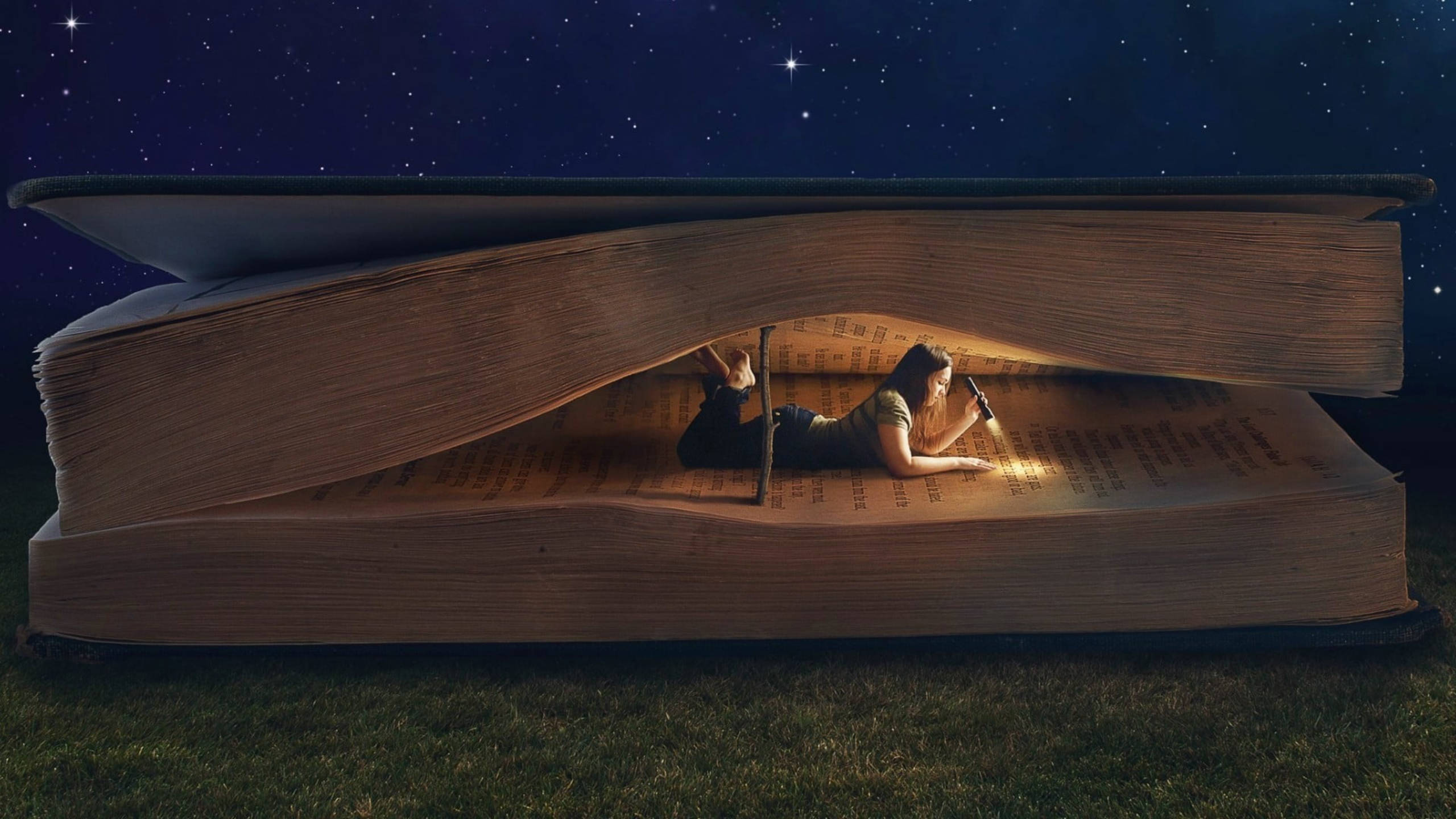 女孩在星空下讀書的同人藝術 壁紙 — 一個人躺在草地上，在星空下的一本巨大打開的書裡閱讀。