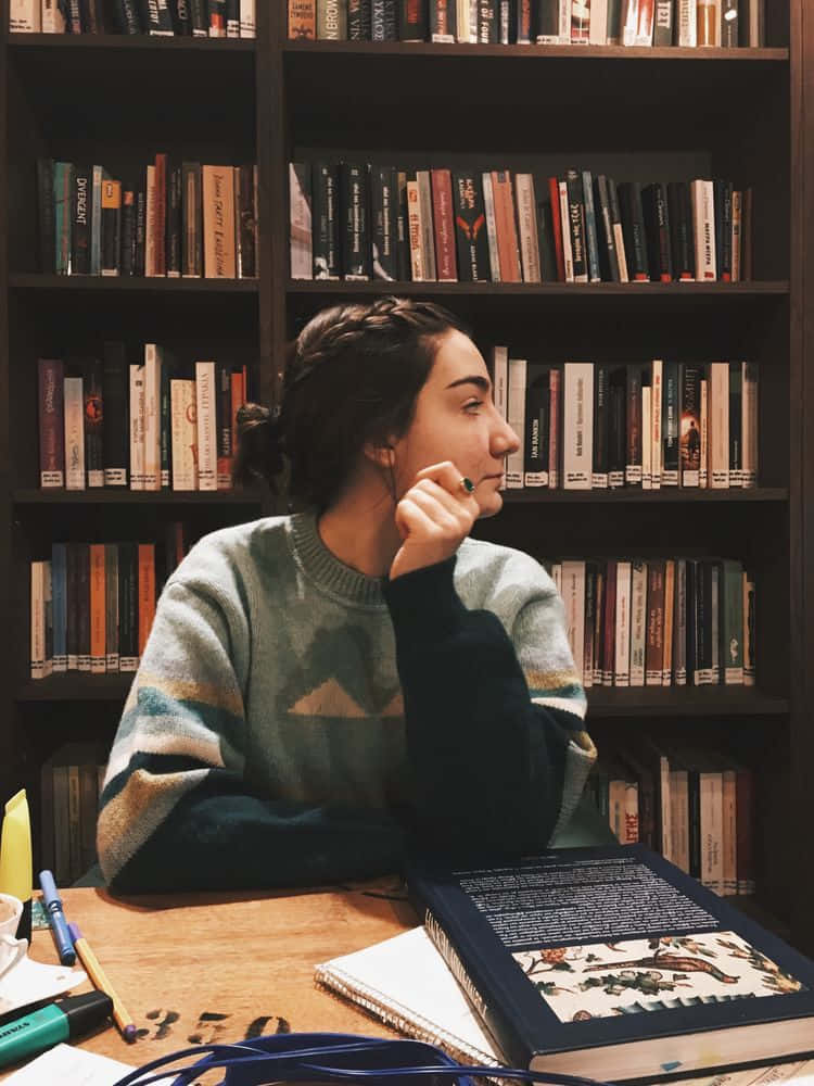 女孩坐在書架前的桌子旁 壁紙