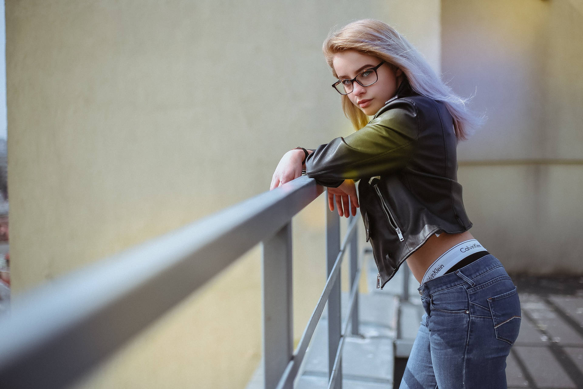 戴眼鏡和皮外套的年輕女士在戶外靠在欄杆上。