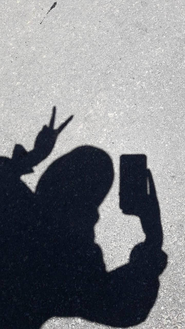 人在路面上做出和平手勢自拍的影子