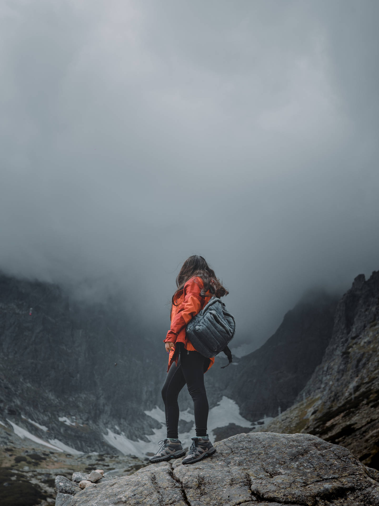 身穿橙色外套的人站在岩石山頂上，下方是霧氣瀰漫的山谷。