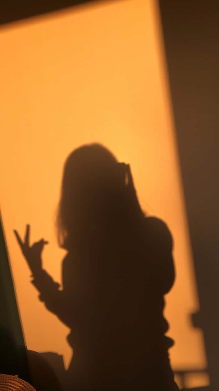 女孩的彩色剪影 壁紙 — 一個人的剪影在黃金時刻對著溫暖發光的窗戶做出和平手勢。