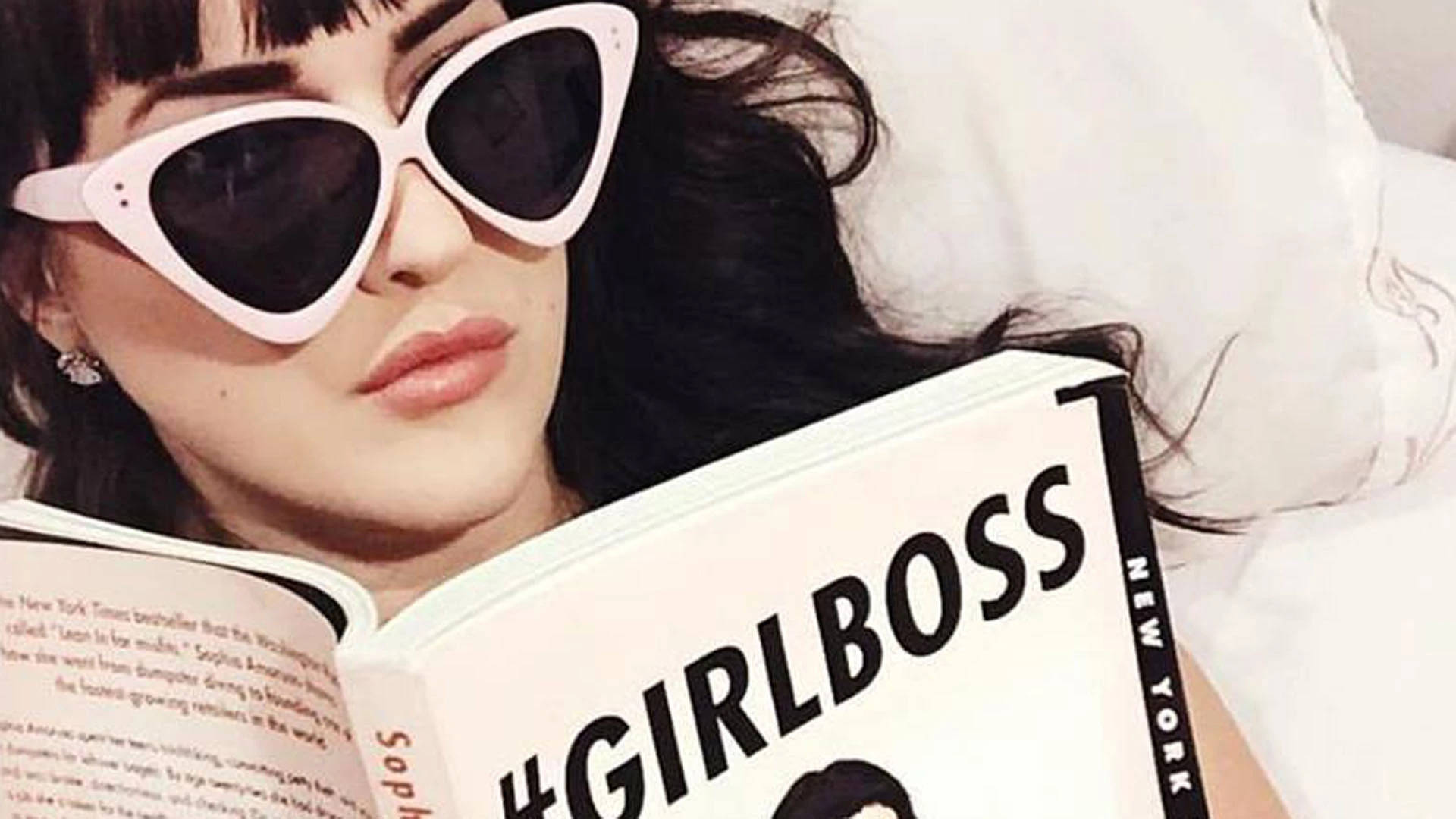 戴白色太陽眼鏡的女性在床上閱讀 Girlboss 書籍