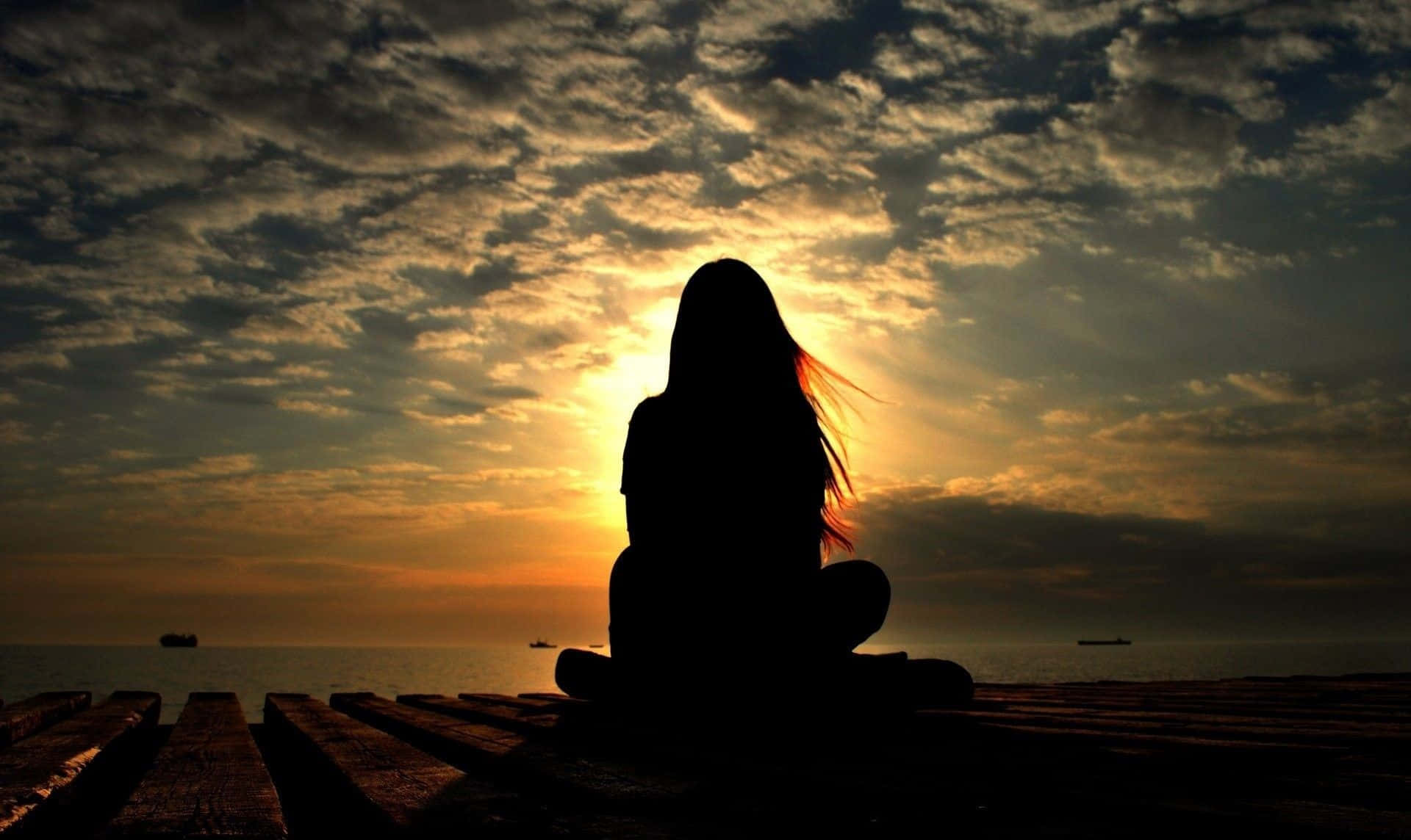 女孩行於黑暗中 壁紙 — 一個人在木碼頭上冥想嘅剪影，金色夕陽光線穿過戲劇性嘅雲層照喺海面上。