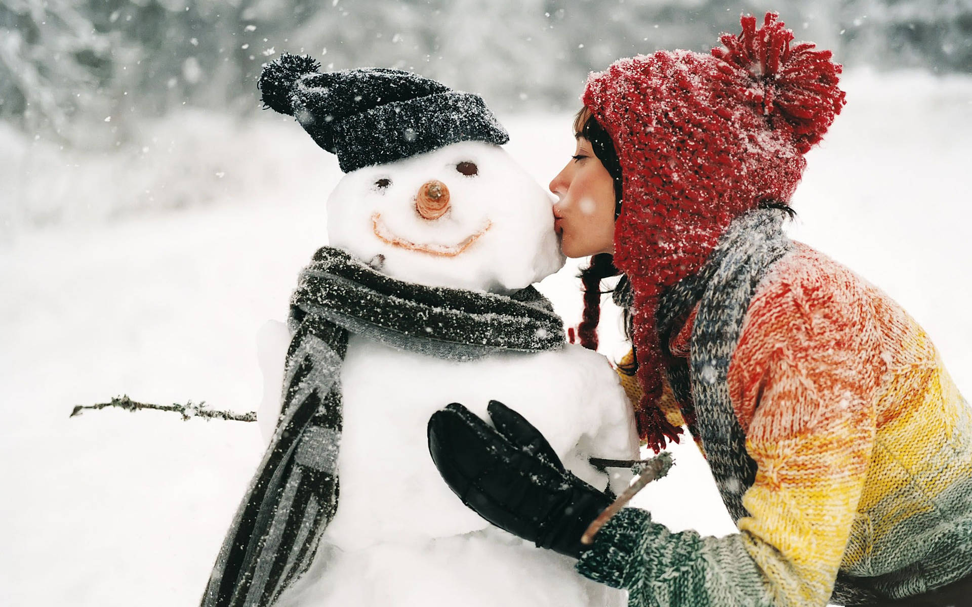 小孩在雪景中親吻雪人，身穿紅帽和彩色毛衣。