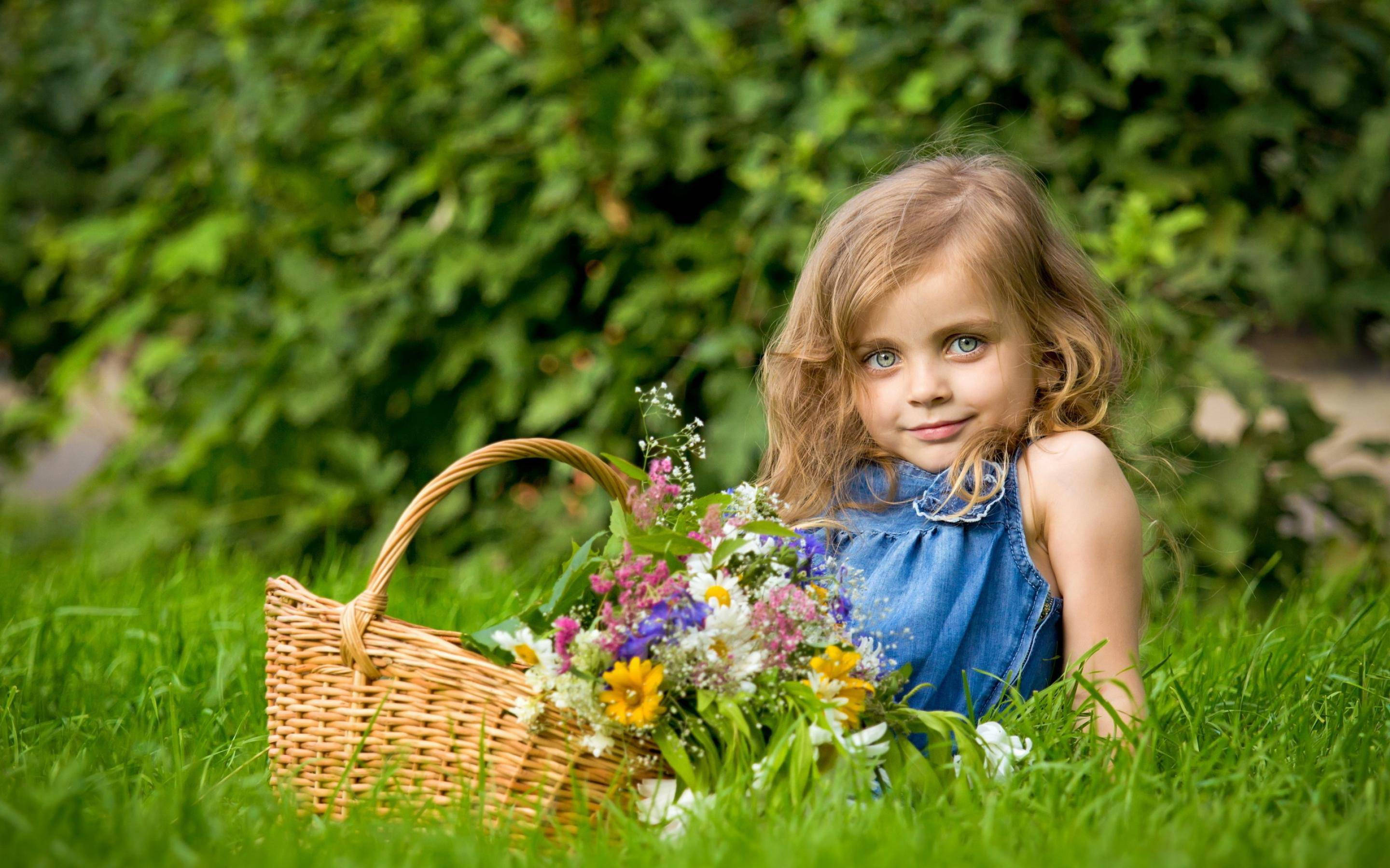 女孩躺在草地上捧著花籃 壁紙 — 一個金髮藍眼的小女孩坐在茂密的綠草地上，旁邊是一個裝滿五顏六色野花的柳條籃。