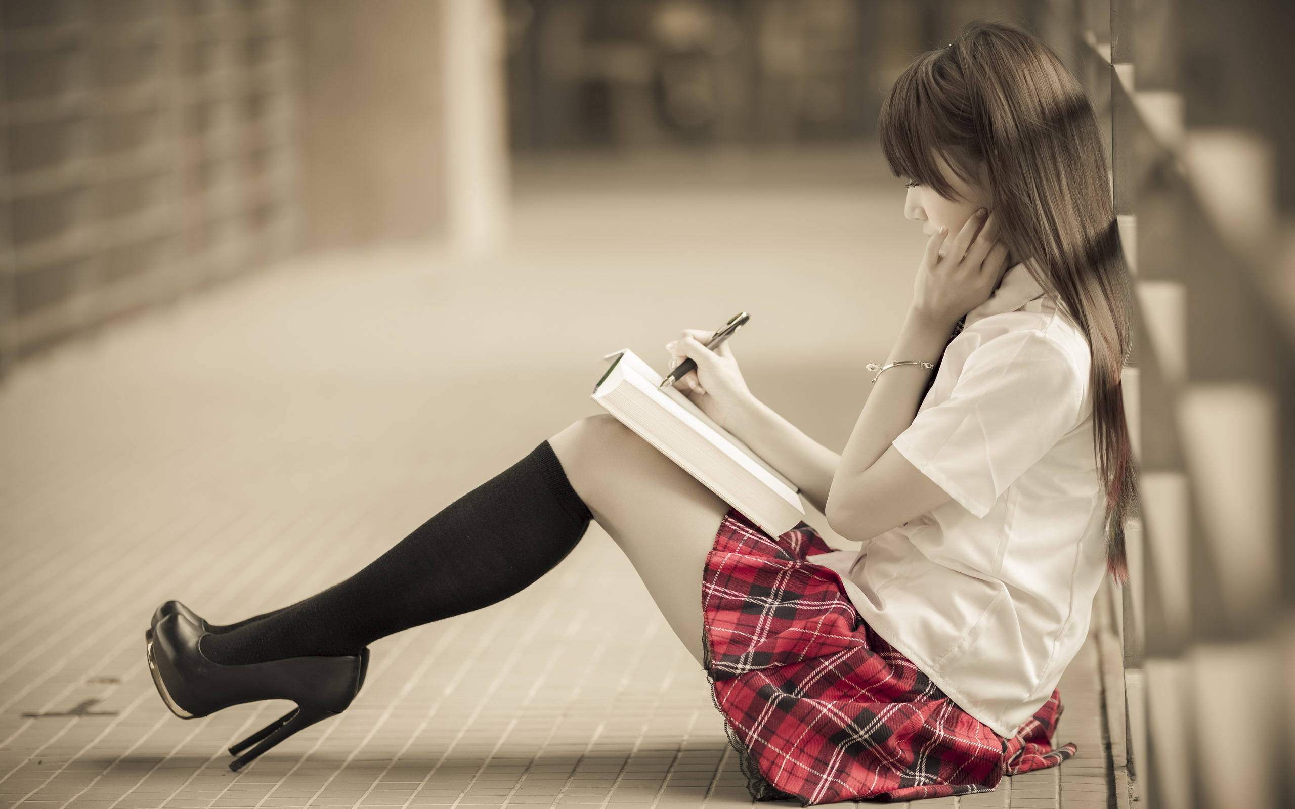 女學生學習 2560x1600 壁紙 — 一位身穿紅色格子裙和黑色高跟鞋的年輕女性坐在瓷磚地上，靠著牆在筆記本上寫字。