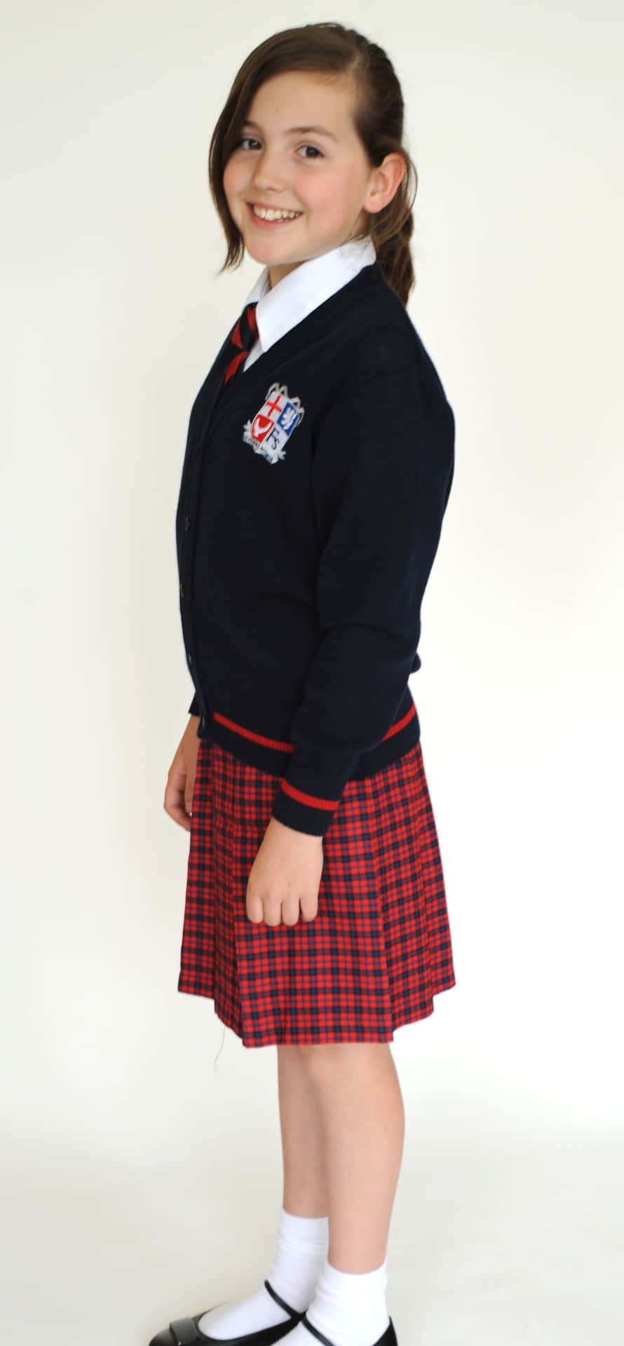 女學生紅裙子照片 壁紙 — 一個微笑的年輕女孩穿著校服，在純白色背景前擺姿勢。
