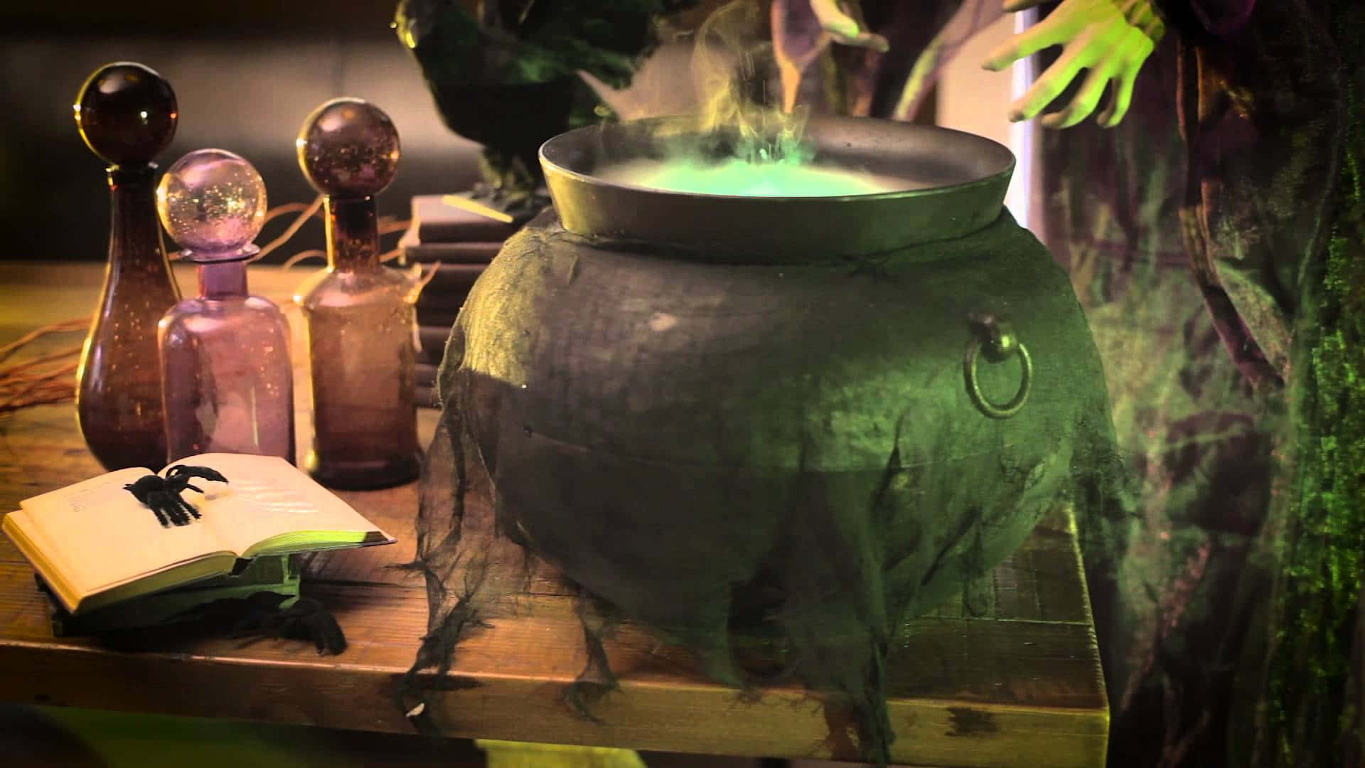 cauldron 桌布 壁紙 — 女巫的大鍋沸騰著發光的綠色藥水，一隻戴著綠色手套的手在攪拌，神秘的瓶子和一本打開的咒語書放在附近。