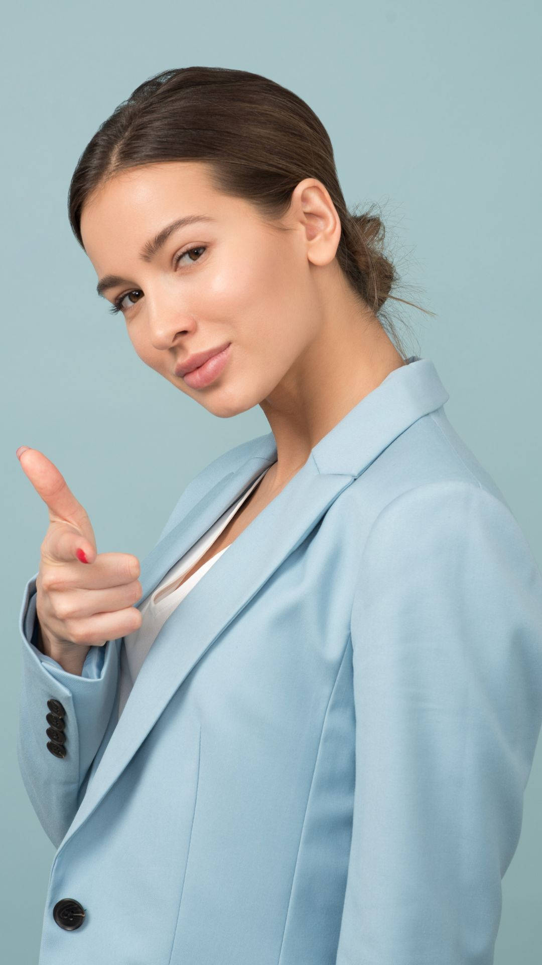 女強人修身西裝 壁紙 — 一位自信的女性穿著淺藍色西裝外套，在柔和的青綠色工作室背景前豎起大拇指。