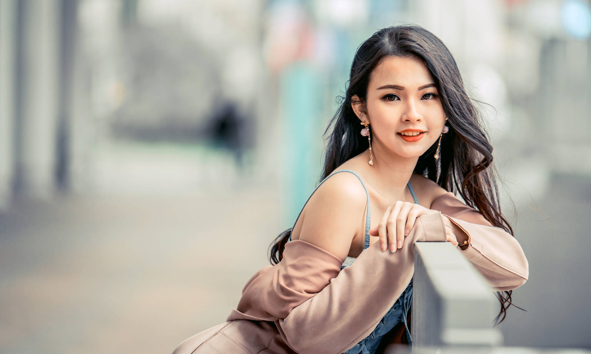 一位穿著粉紅色外套的微笑女性在城市街道上倚靠欄杆。