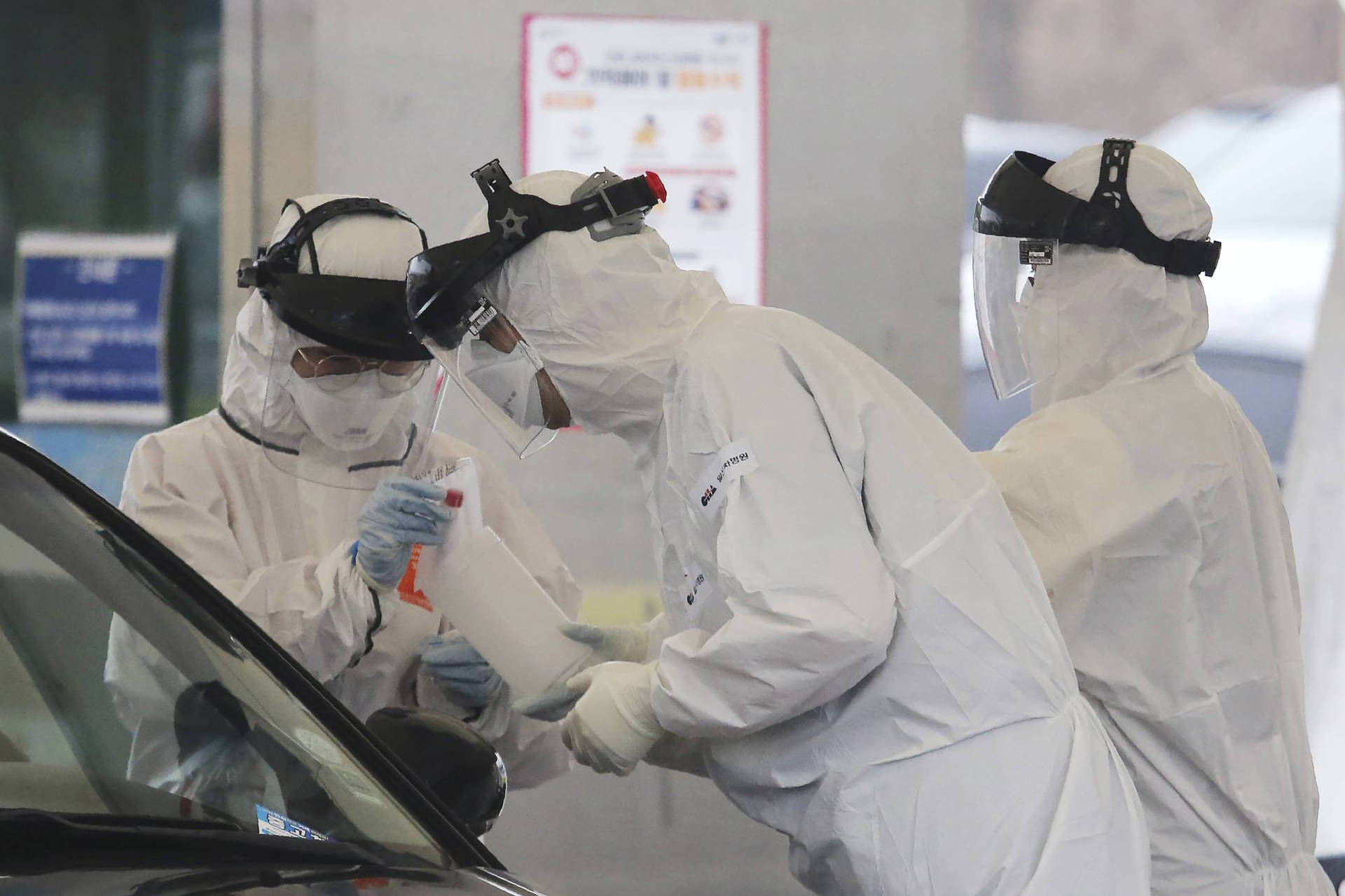 穿著防護裝備的醫護人員在免下車檢測期間從汽車收集樣本。