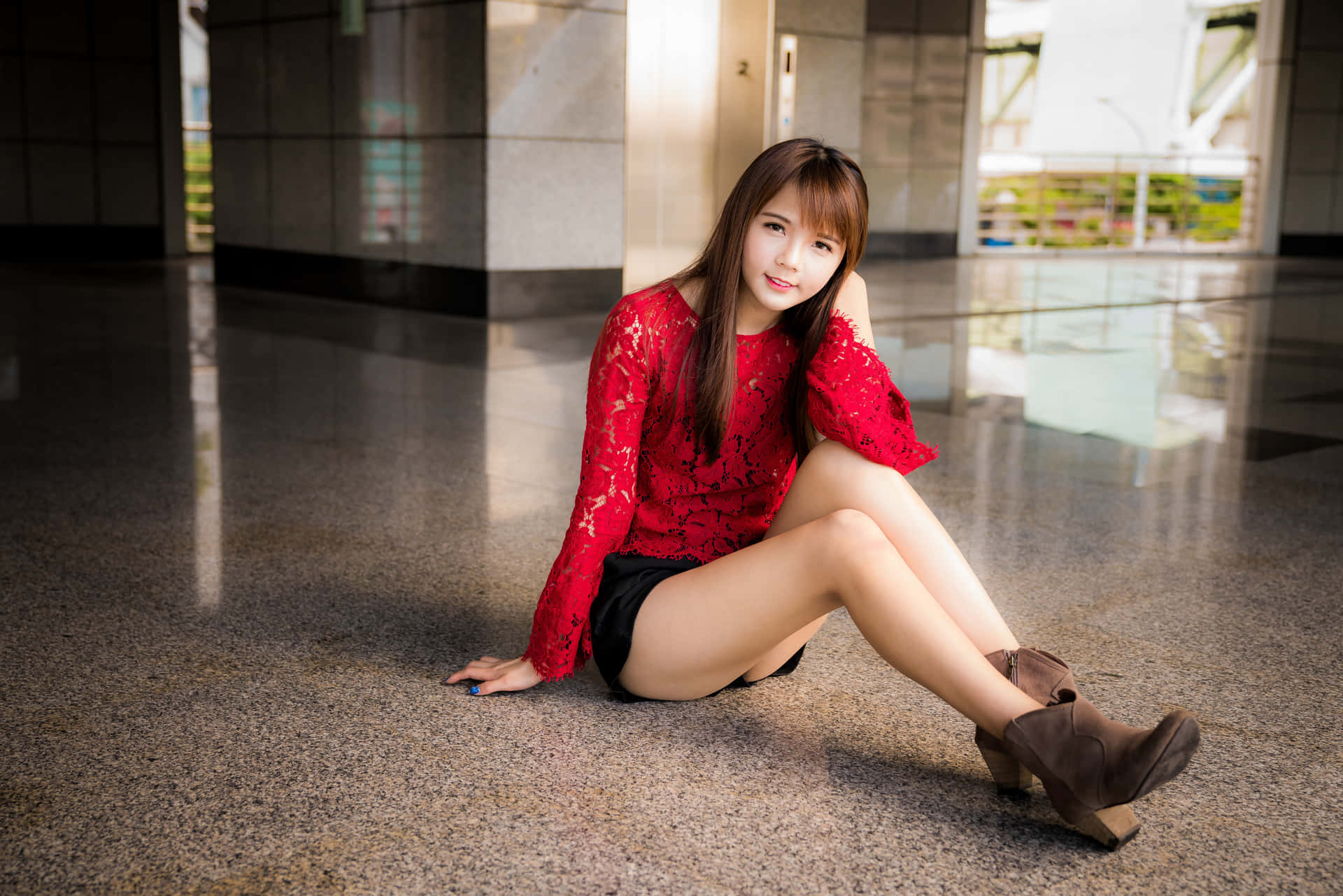 身穿紅色蕾絲上衣的年輕女士坐在室內拋光地板上