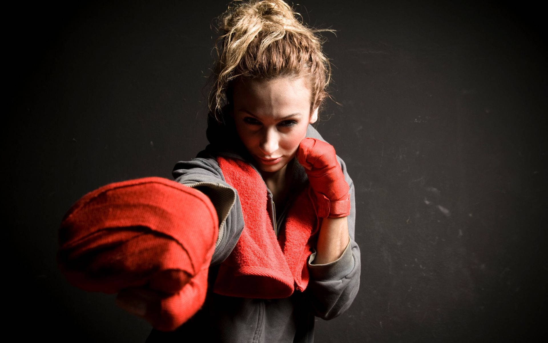 女拳擊手戴紅色手套在黑暗攝影棚中出拳。