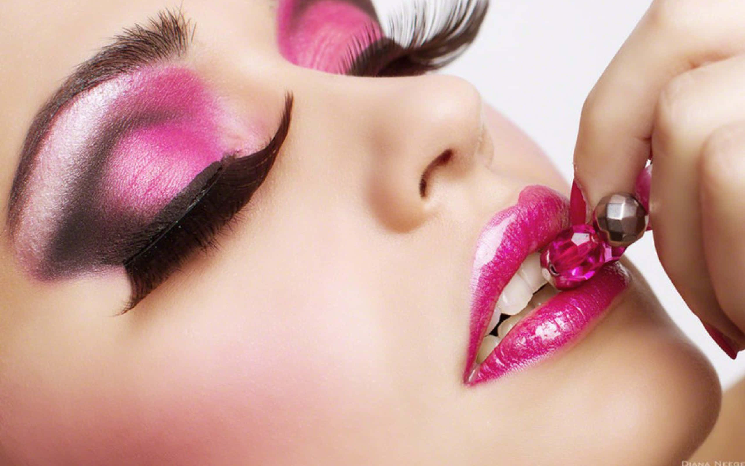 Pink Makeup 桌布 壁紙 — 女性臉部特寫，帶有鮮豔的粉紅色眼影和嘴唇，她正小心翼翼地將珠寶飾品放在嘴邊。