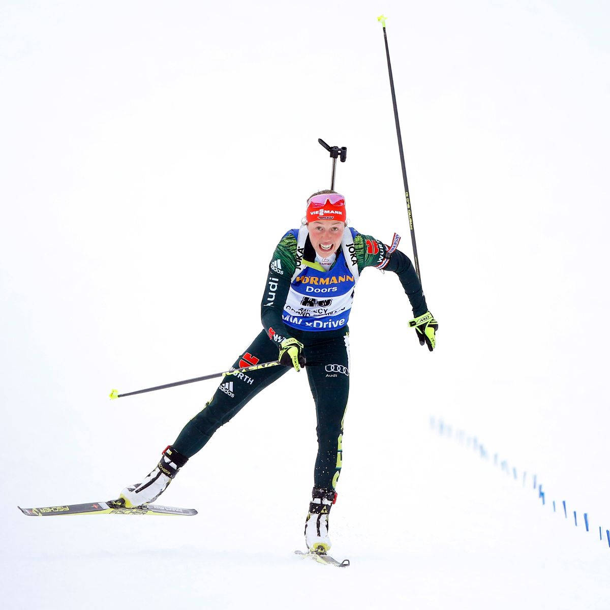 女性越野滑雪射擊運動員疾馳下坡 壁紙 — 一位堅定的女子越野滑雪選手，用雪杖撐地，滑雪板刃劃過白色雪粉，奮力向前。