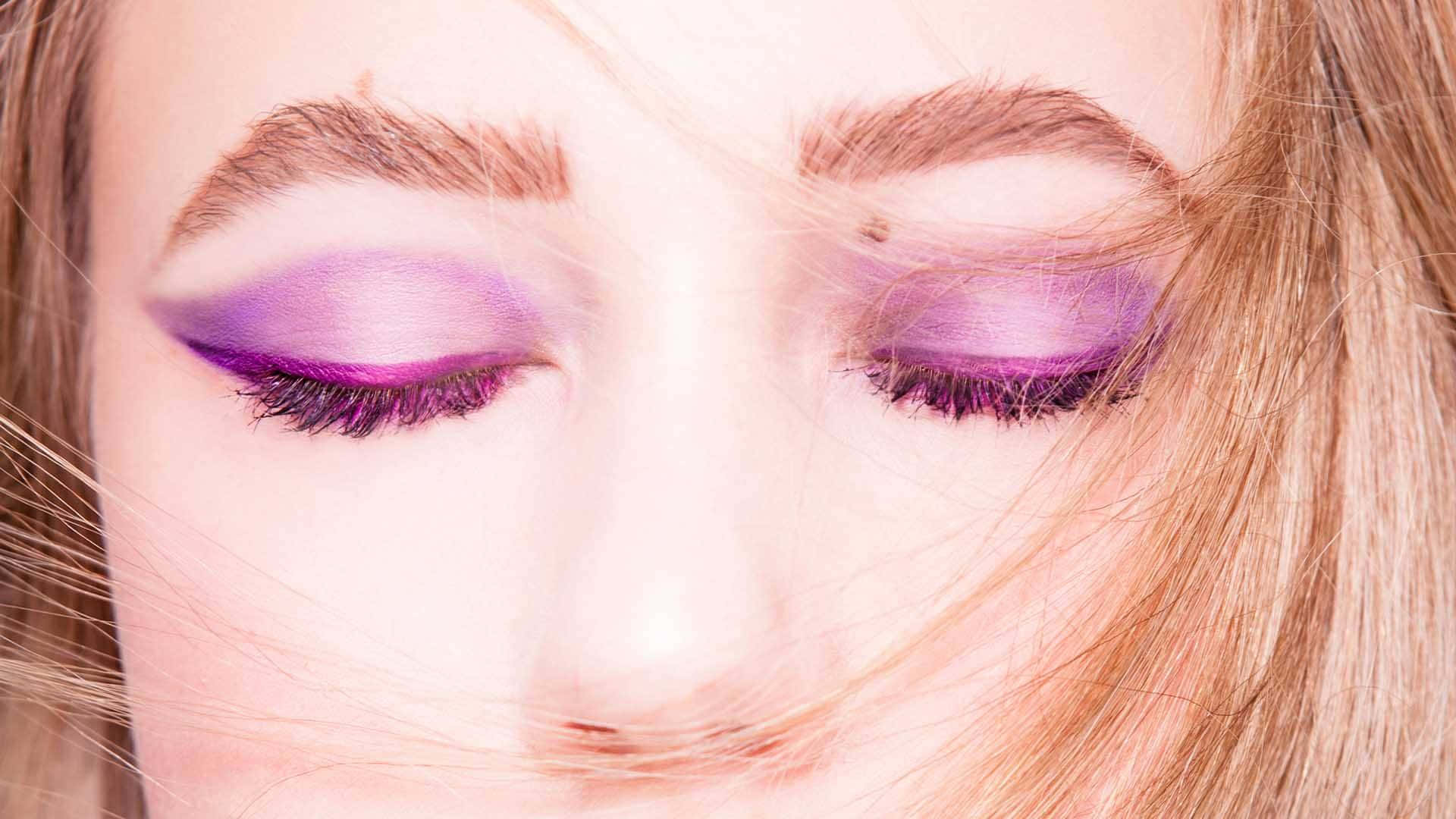 Purple Eye Shadow 桌布 壁紙 — 女性閉上眼睛的特寫，飾有充滿活力的紫色眼影和睫毛，金色頭髮輕輕吹過她的臉龐。
