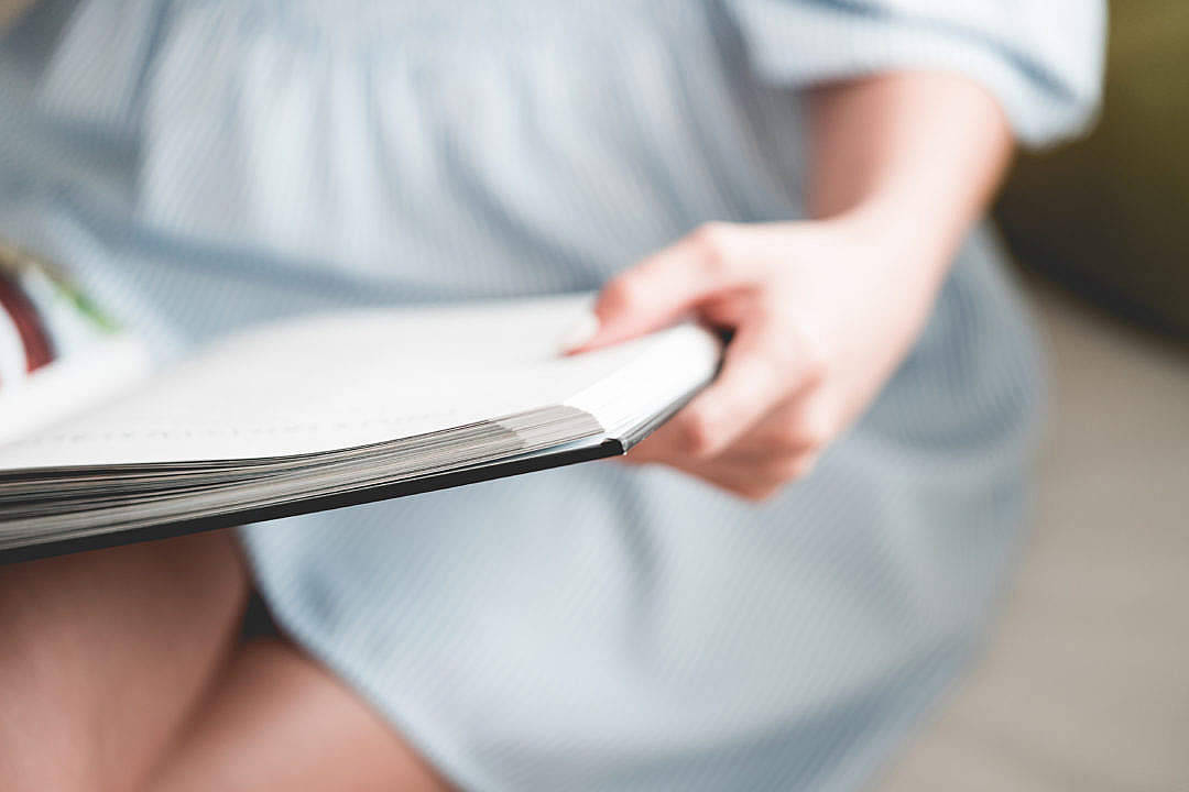 穿藍色連衣裙的人在室內閱讀時拿著打開的書。