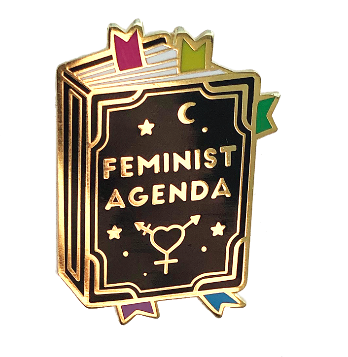 女權議程書形琺瑯胸針 壁紙 — 一個閃亮的琺瑯別針，形狀像一本名為「FEMINIST AGENDA」的書，帶有金色邊飾、星星、月亮和性別符號。