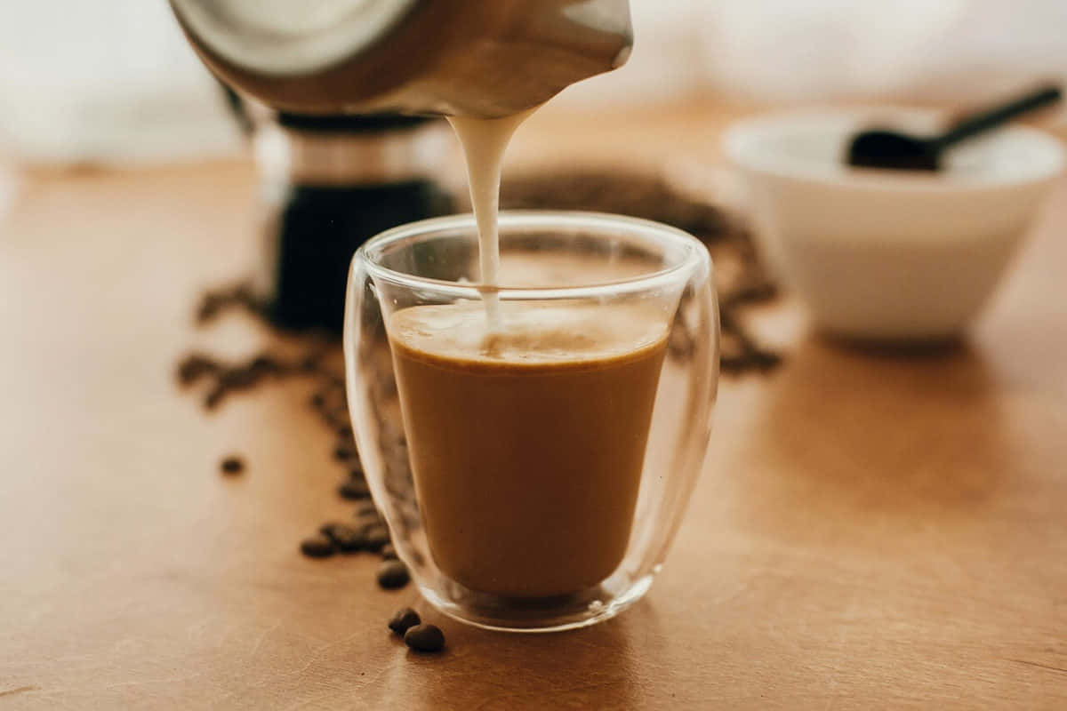 Milk And Coffee 桌布 壁紙 — 奶油咖啡倒入雙層玻璃杯中，放在被咖啡豆包圍的木桌上。