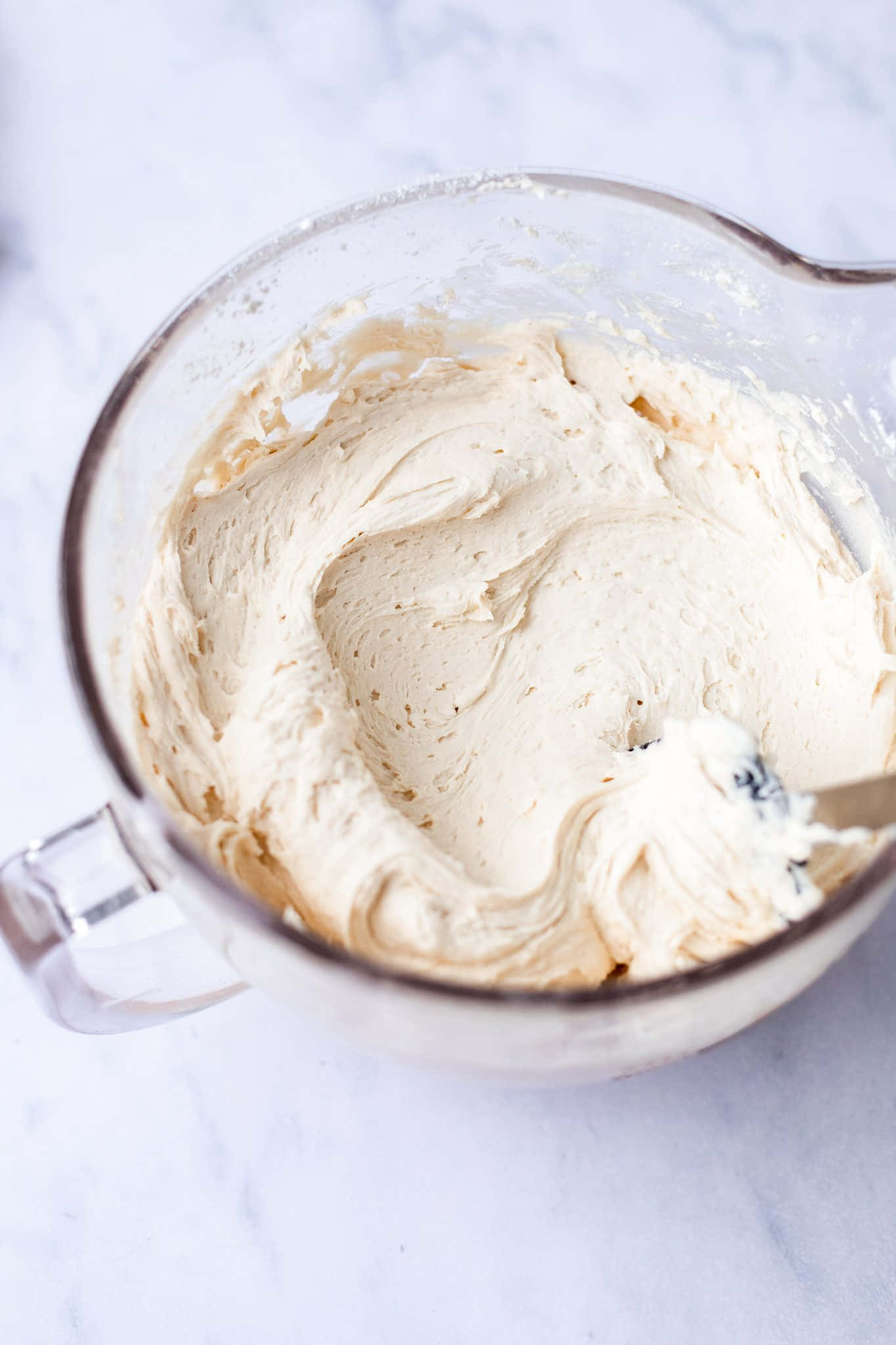 Buttercream 桌布 壁紙 — 奶油淡黃色糖霜在透明玻璃攪拌碗中旋轉，置於白色大理石表面上。