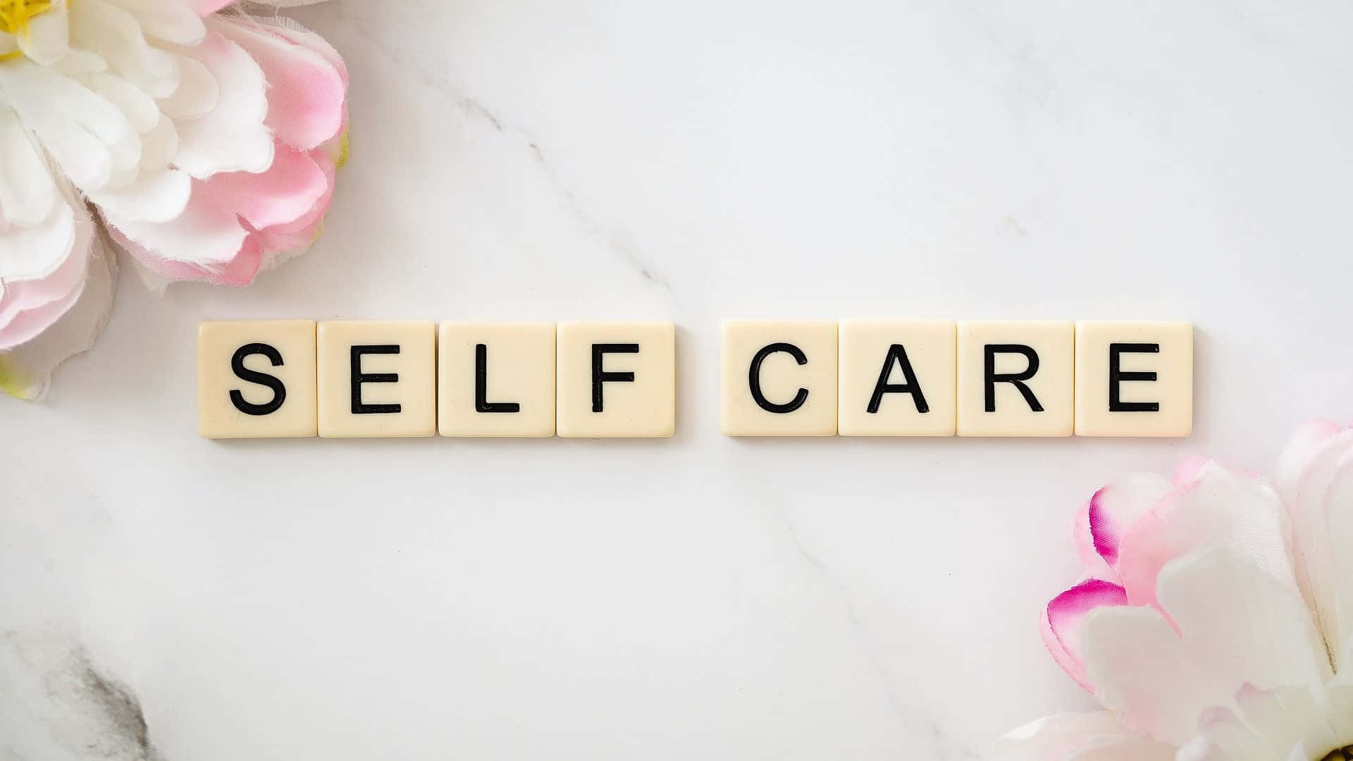 Self Care 桌布 壁紙 — 奶油色瓷磚拼出SELF CARE，放置在白色大理石表面上，兩側有柔和的粉紅色和白色花朵。